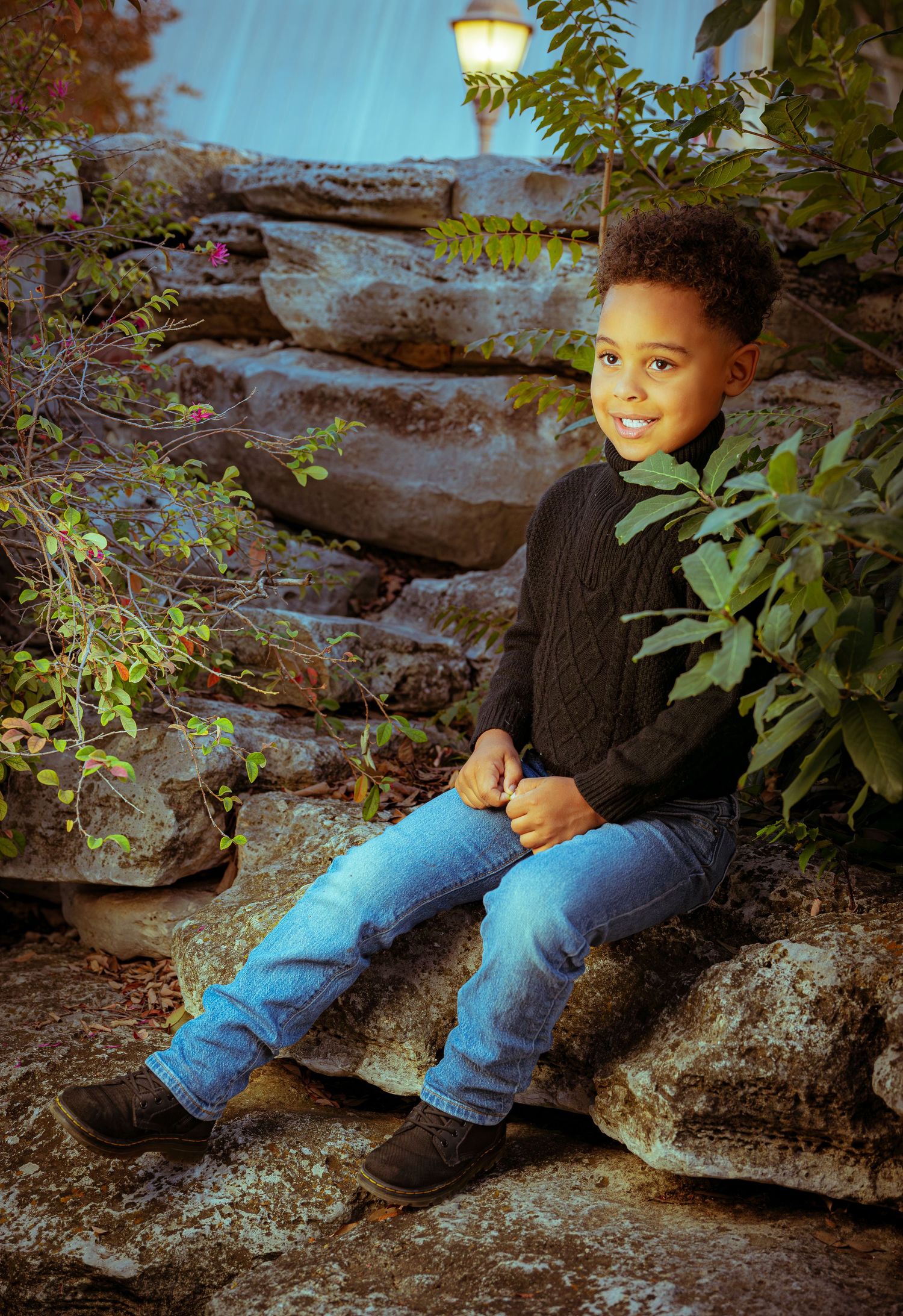 A figure sits on stone steps surrounded by lush greenery and illuminated by a glowing lamp at dusk.