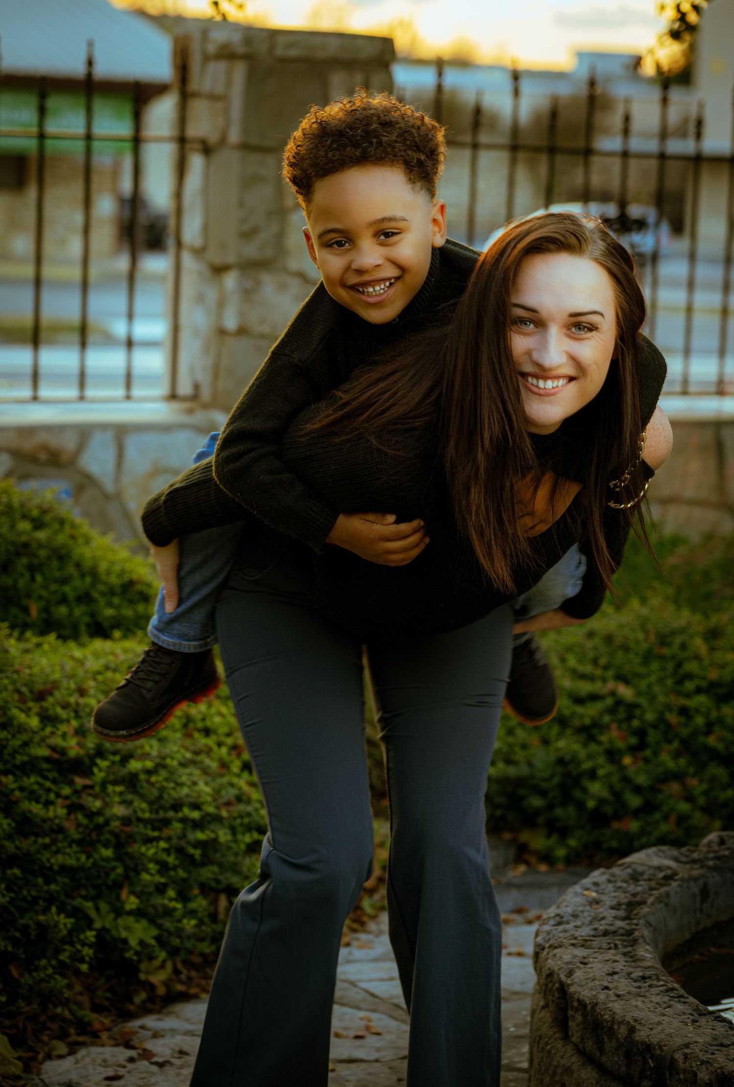 Two friends share a playful piggyback ride moment outdoors against a sunlit background.