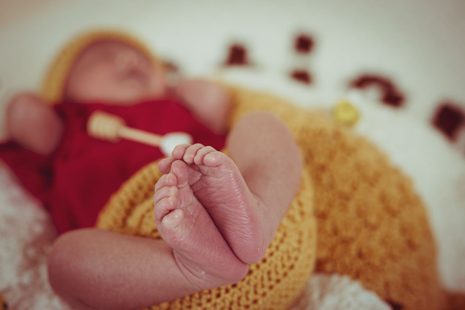 Close-up of newborn baby feet wrapped in a yellow knit blanket with a red outfit in soft focus background.