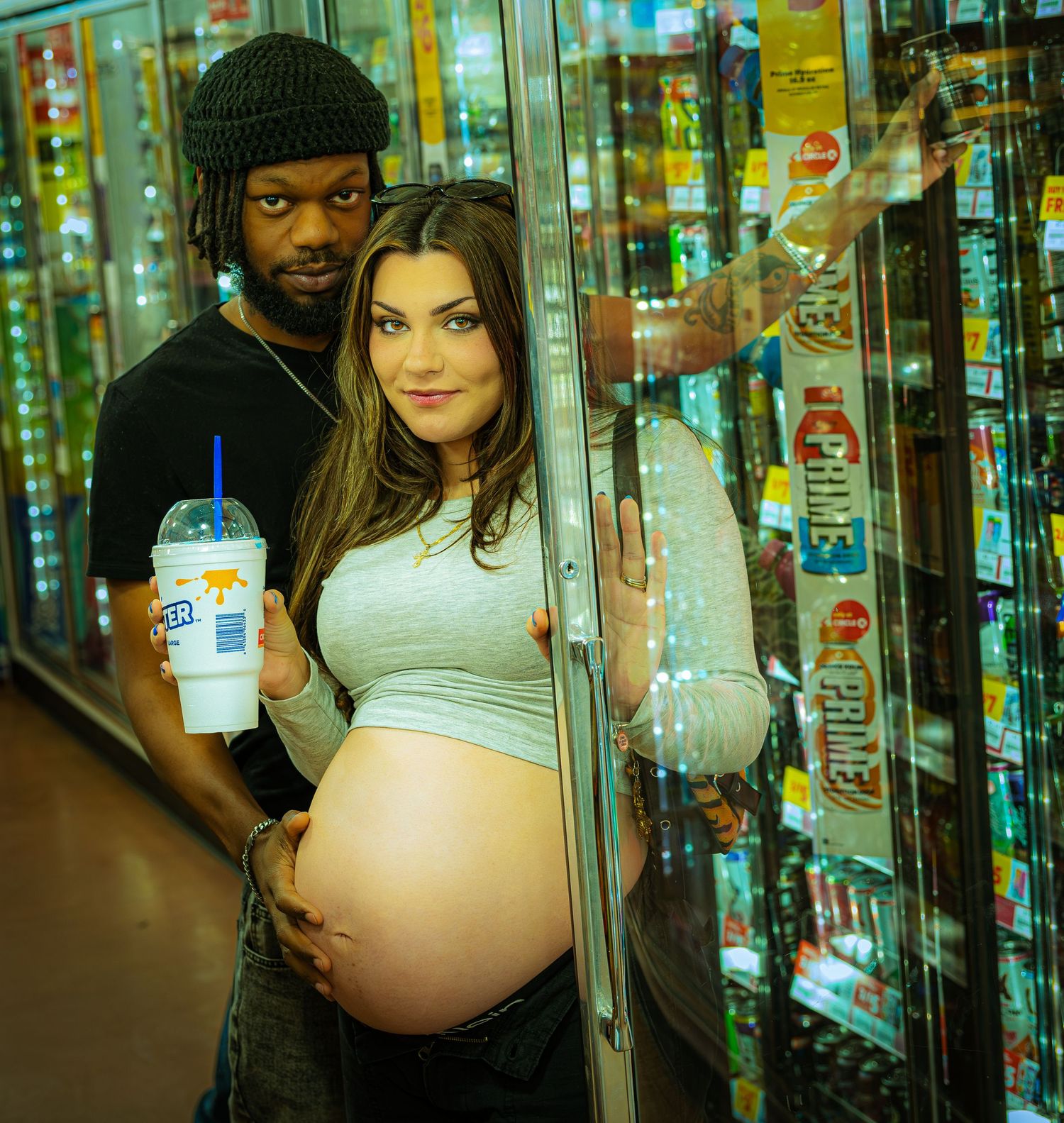 Couple standing in front of illuminated convenience store coolers with drinks.