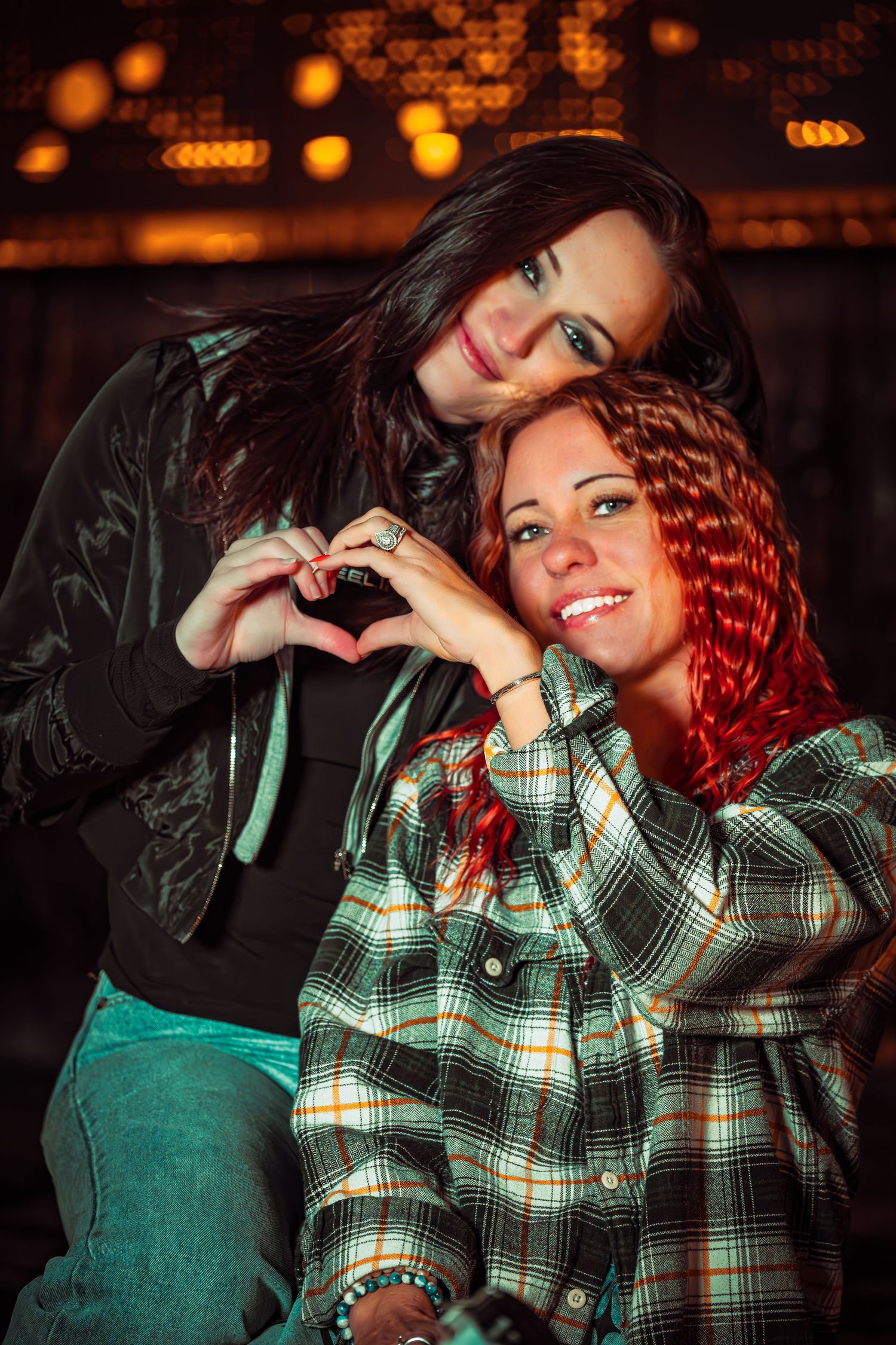 A person wearing a plaid shirt and green overalls poses playfully in a dimly lit setting with bokeh lights in the background.