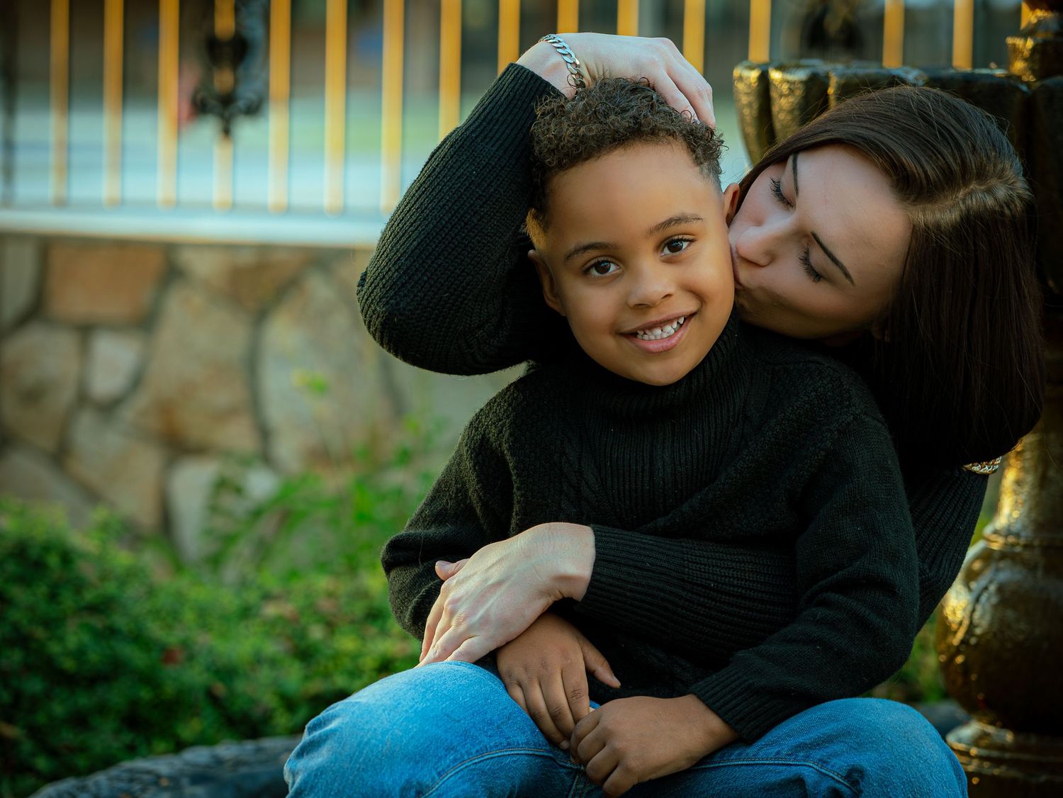 A loving embrace between parent and child sitting outdoors during a warm sunset.