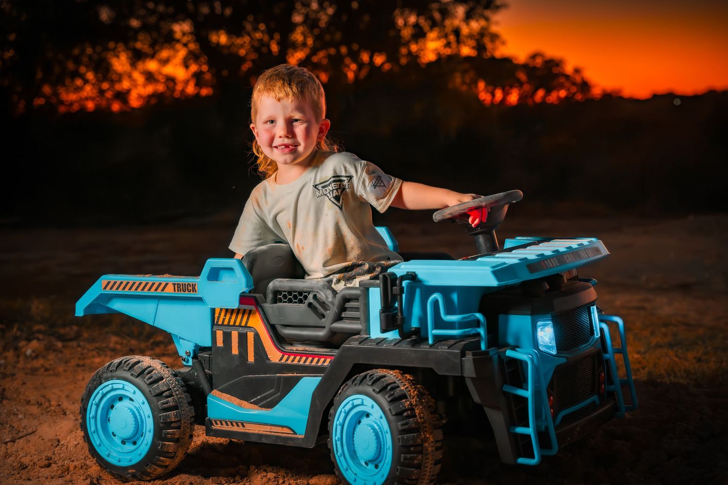 Toy construction vehicle photographed against stunning orange sky at dusk.