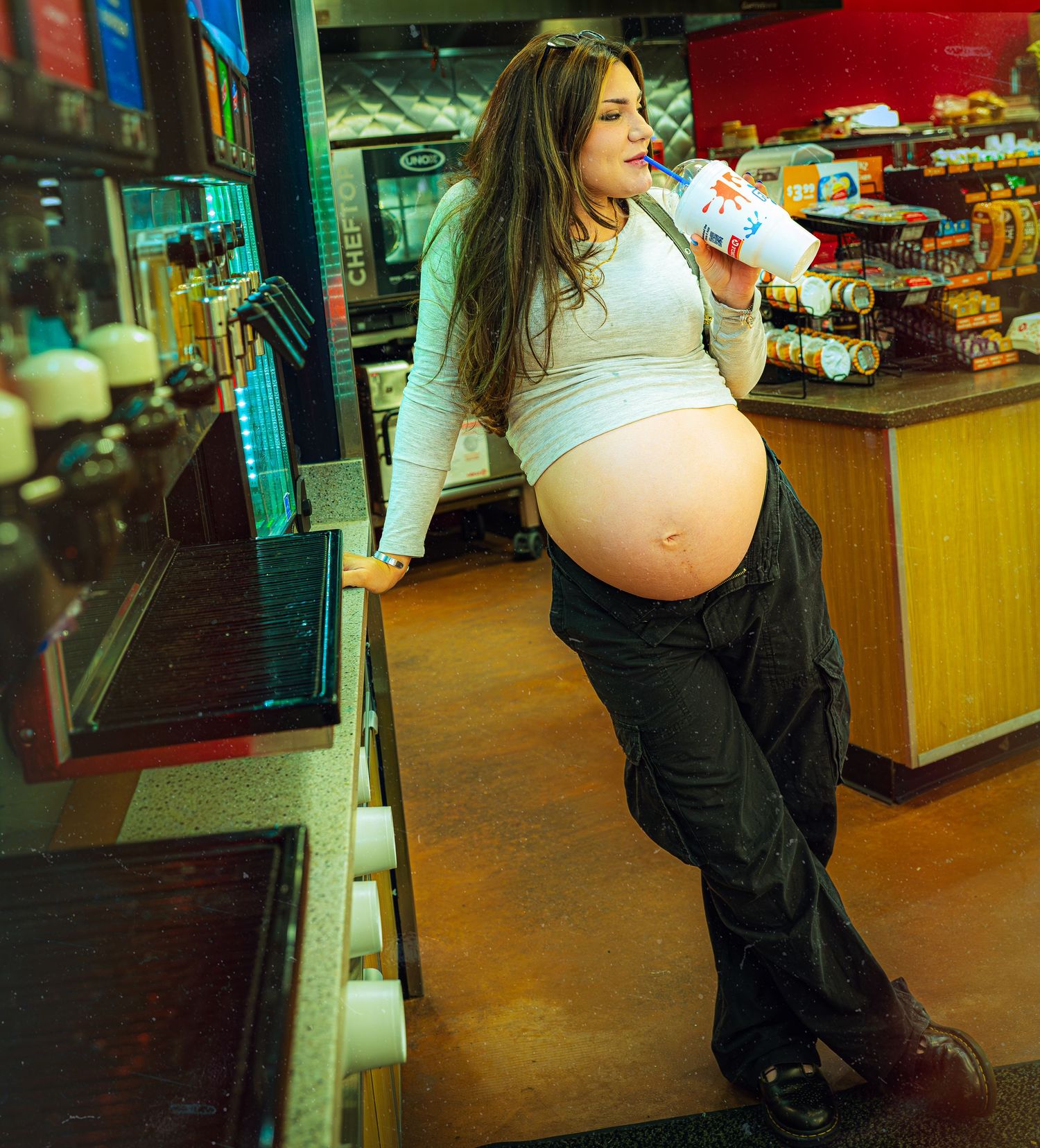 A pregnant person in casual attire browses items at a convenience store.