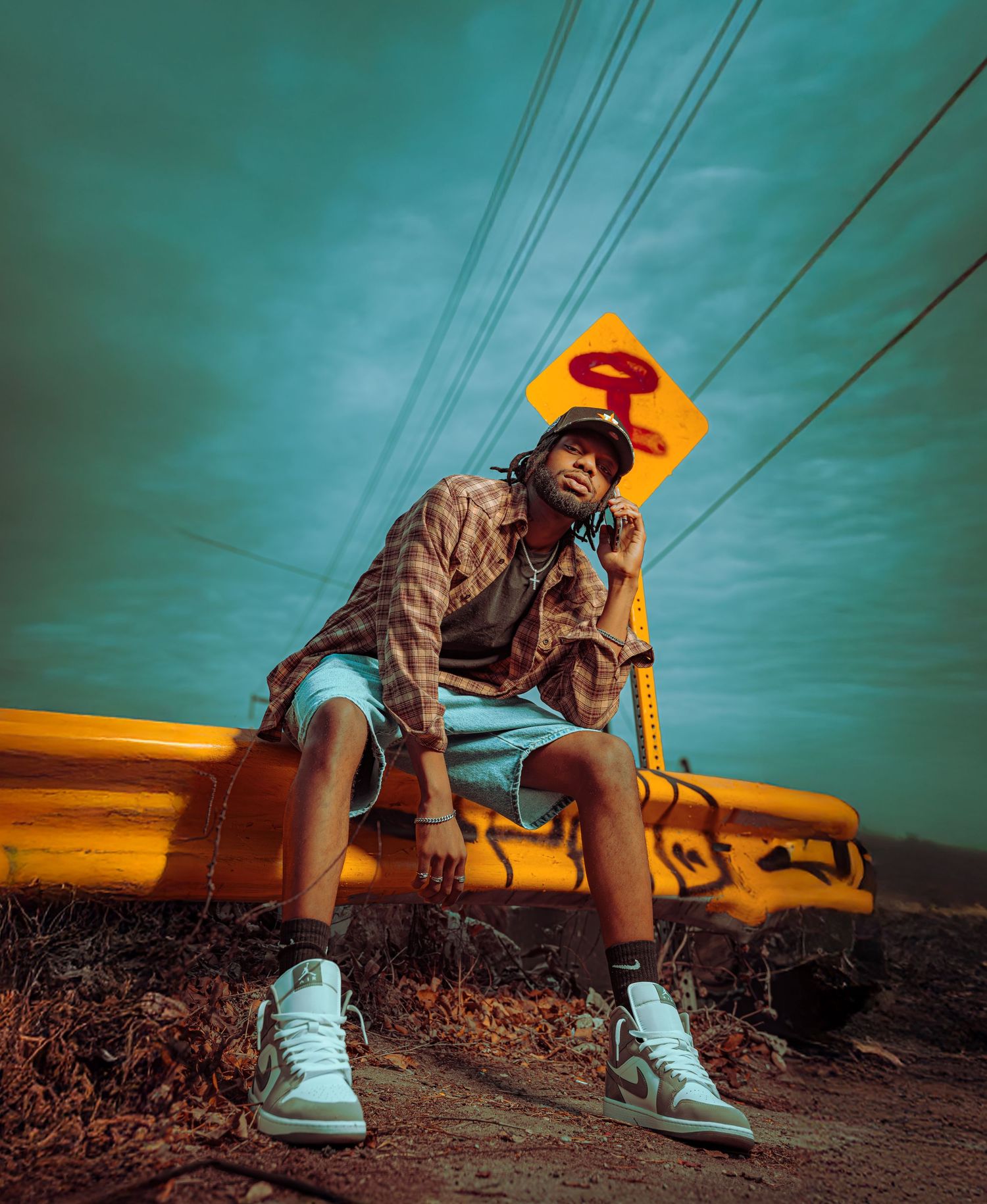 A person in shorts and sneakers sits on a yellow power line against a dramatic turquoise sky at sunset.
