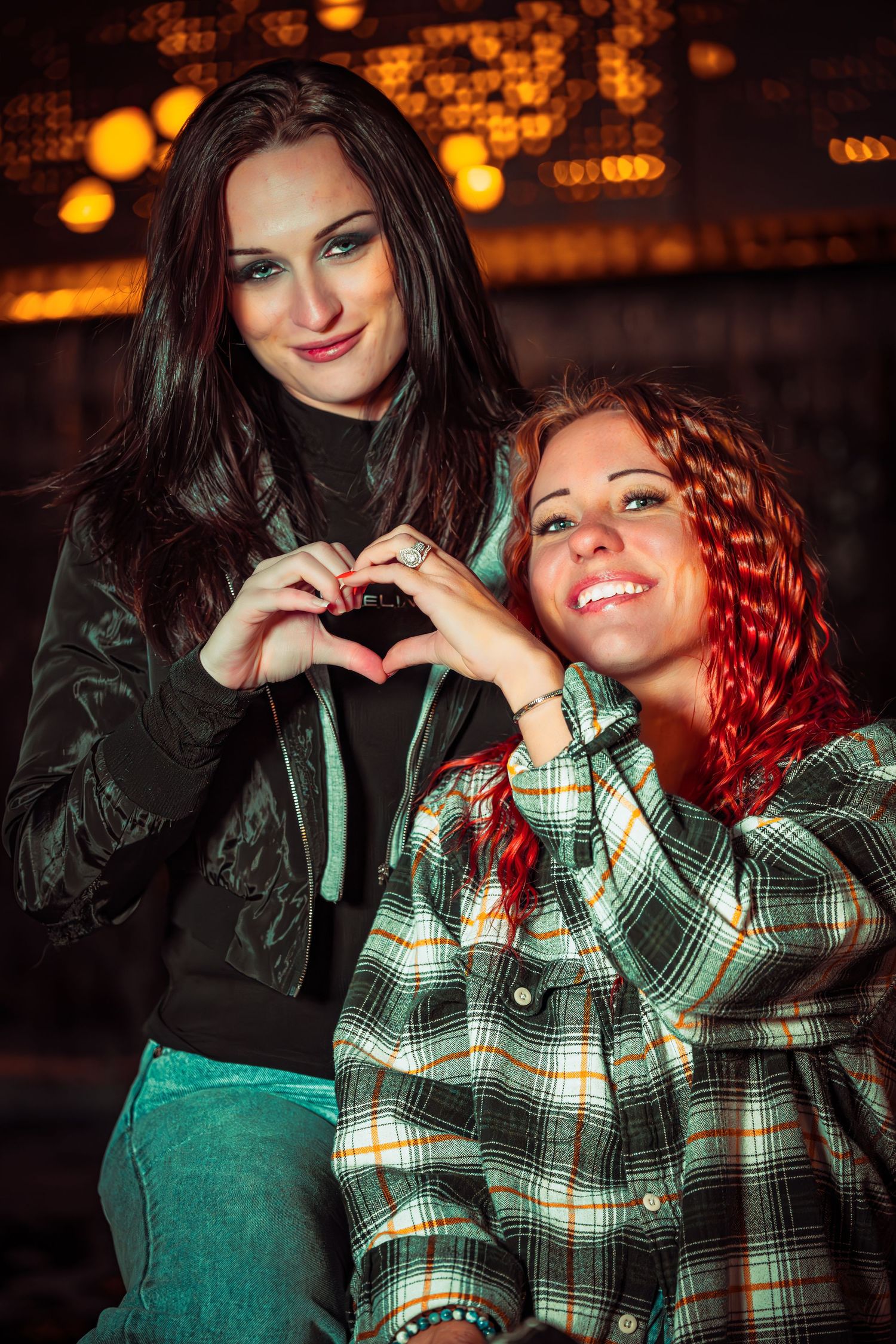 Two people in contrasting outfits share a playful moment against a dark background with warm lighting.