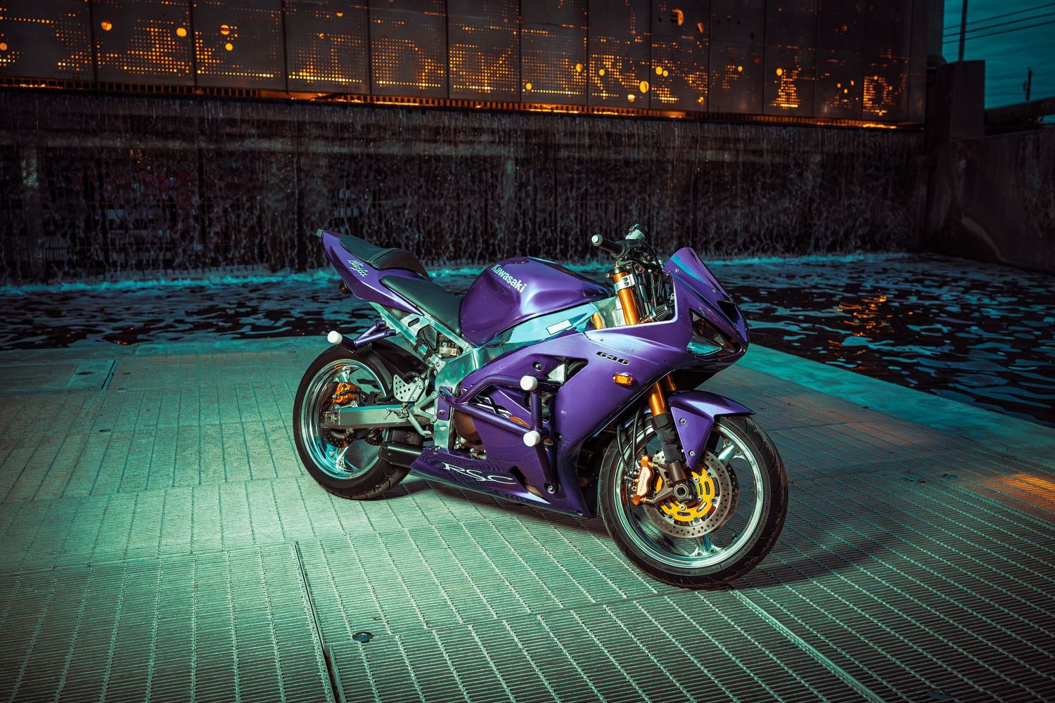 Custom motorcycle with purple neon lighting photographed at night on a brick street.
