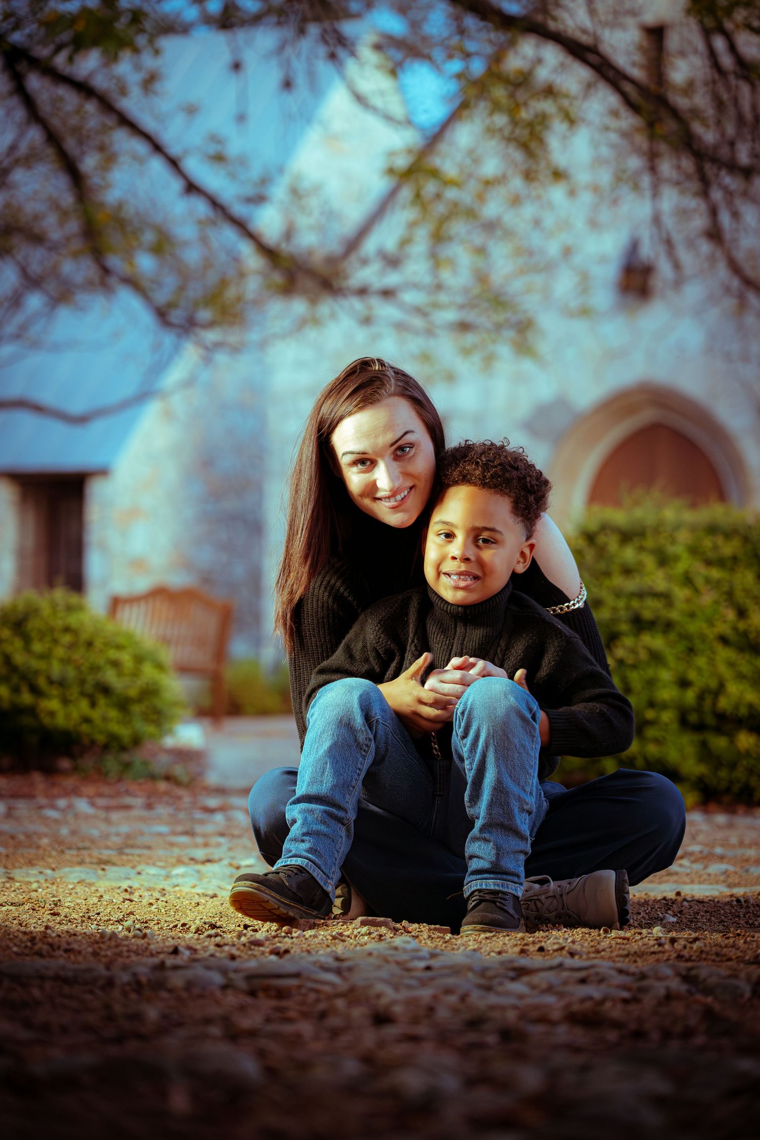 Two people share a playful moment while lying on autumn leaves on the ground with a soft bokeh background effect.