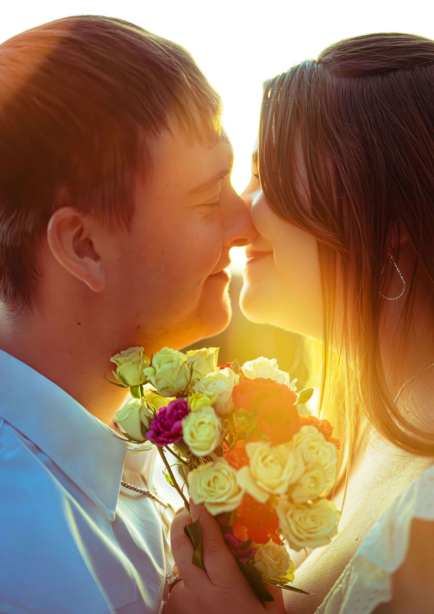 Romantic silhouette of a couple kissing with flowers and golden sunset light shining behind them.