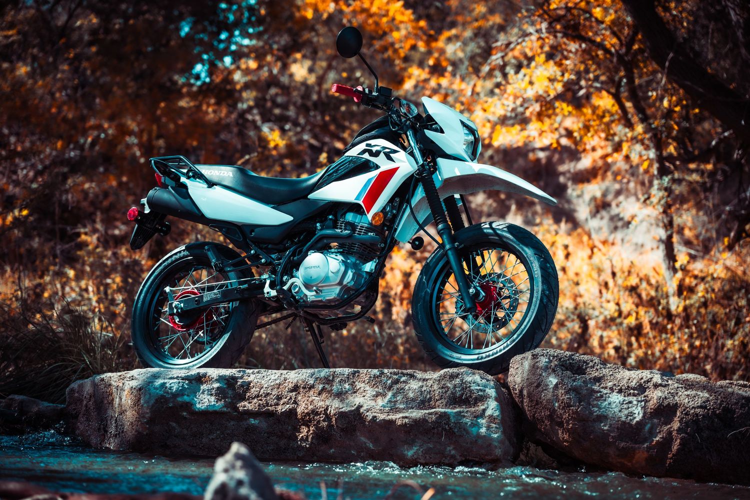 Off-road motorcycle showcased on rocky ledge with dramatic orange and teal color contrast.