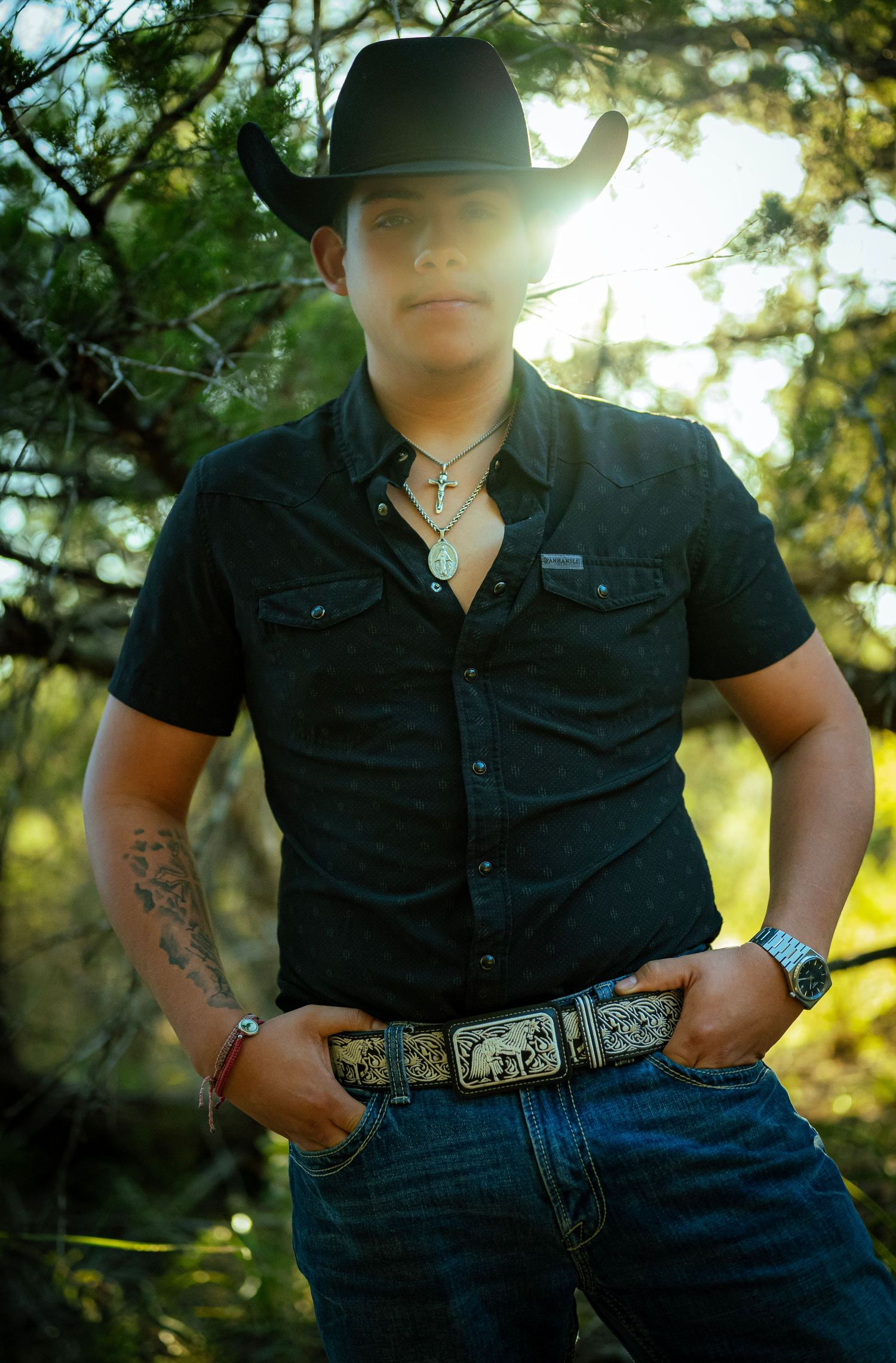 Western-style portrait series showing black shirt, decorative belt buckle, and cowboy hat against natural outdoor setting.
