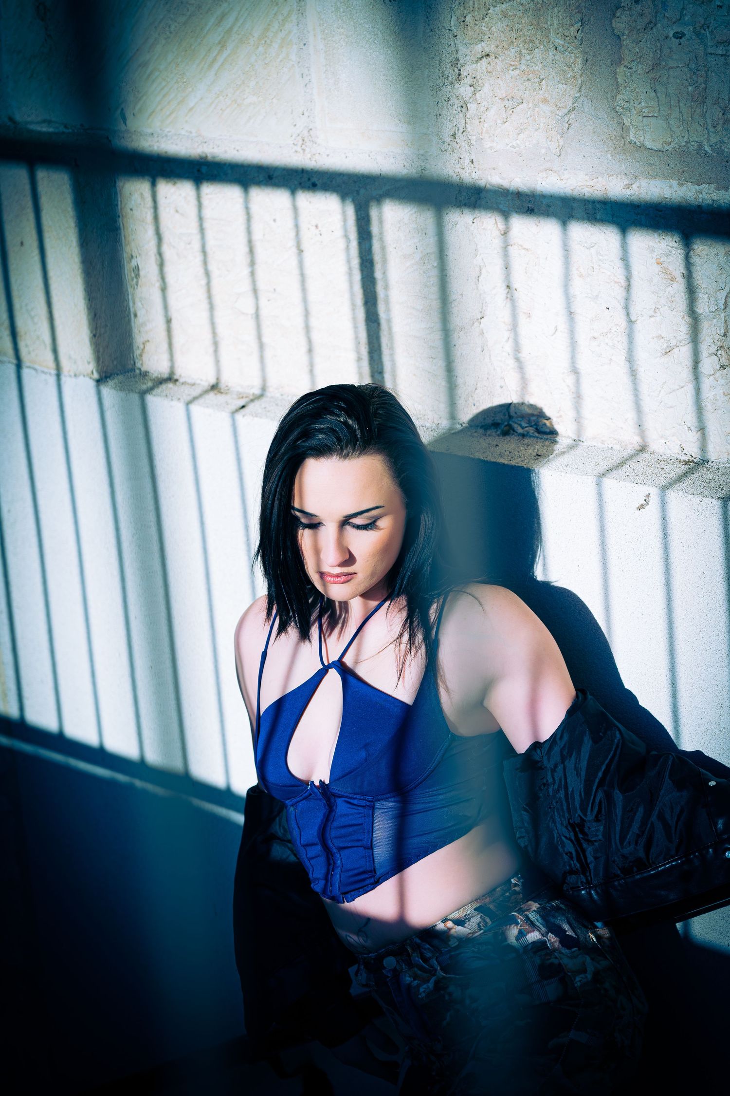 Dramatic indoor photoshoot with blue clothing and moody lighting through window blinds.