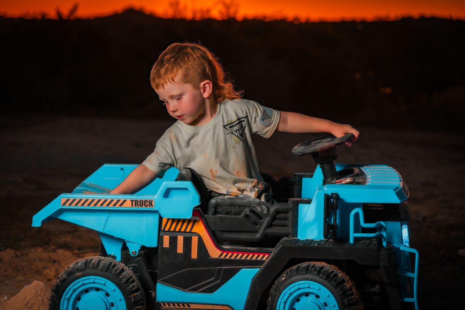 Blue toy construction truck against dark background with orange sunset glow.