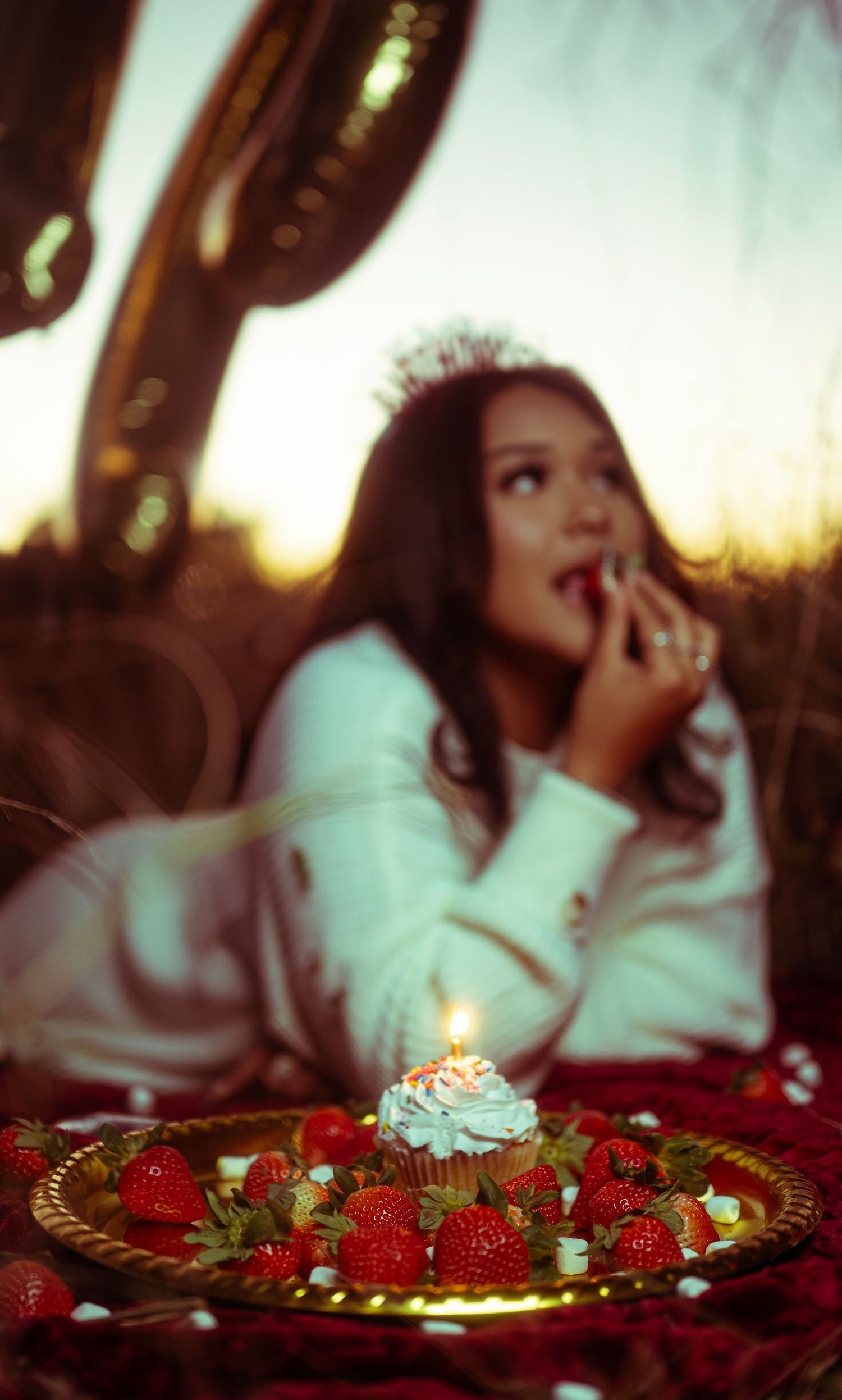 A decorative plate of fresh strawberries and whipped cream sits in front of someone in a white sweater at sunset.