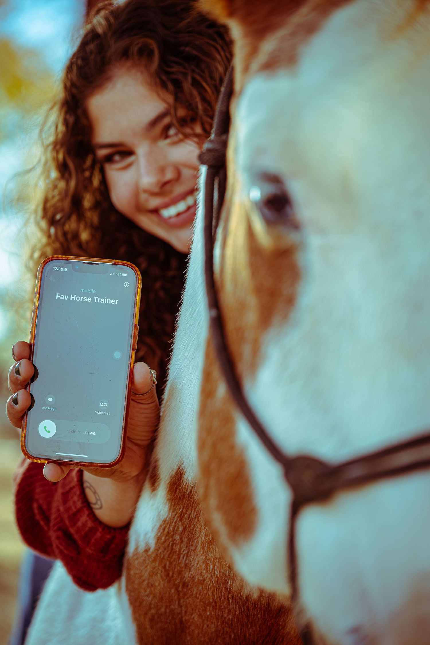 Person in red sweater showing phone screen while standing next to white horse in soft focus shot.