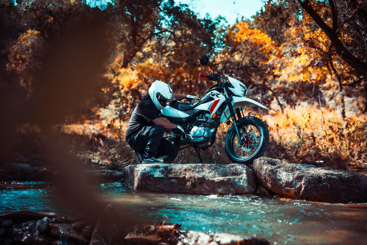 Motorcycle photographed in natural setting with cascading water and warm autumn tones.