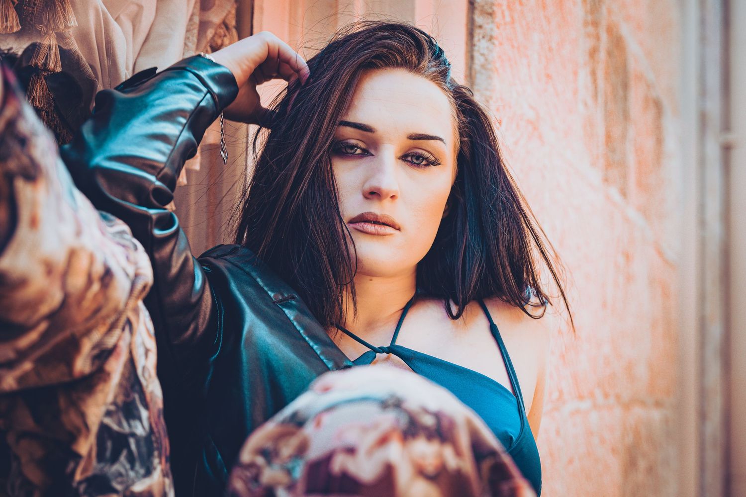 Fashion portrait against textured wall with leather jacket and dramatic lighting.
