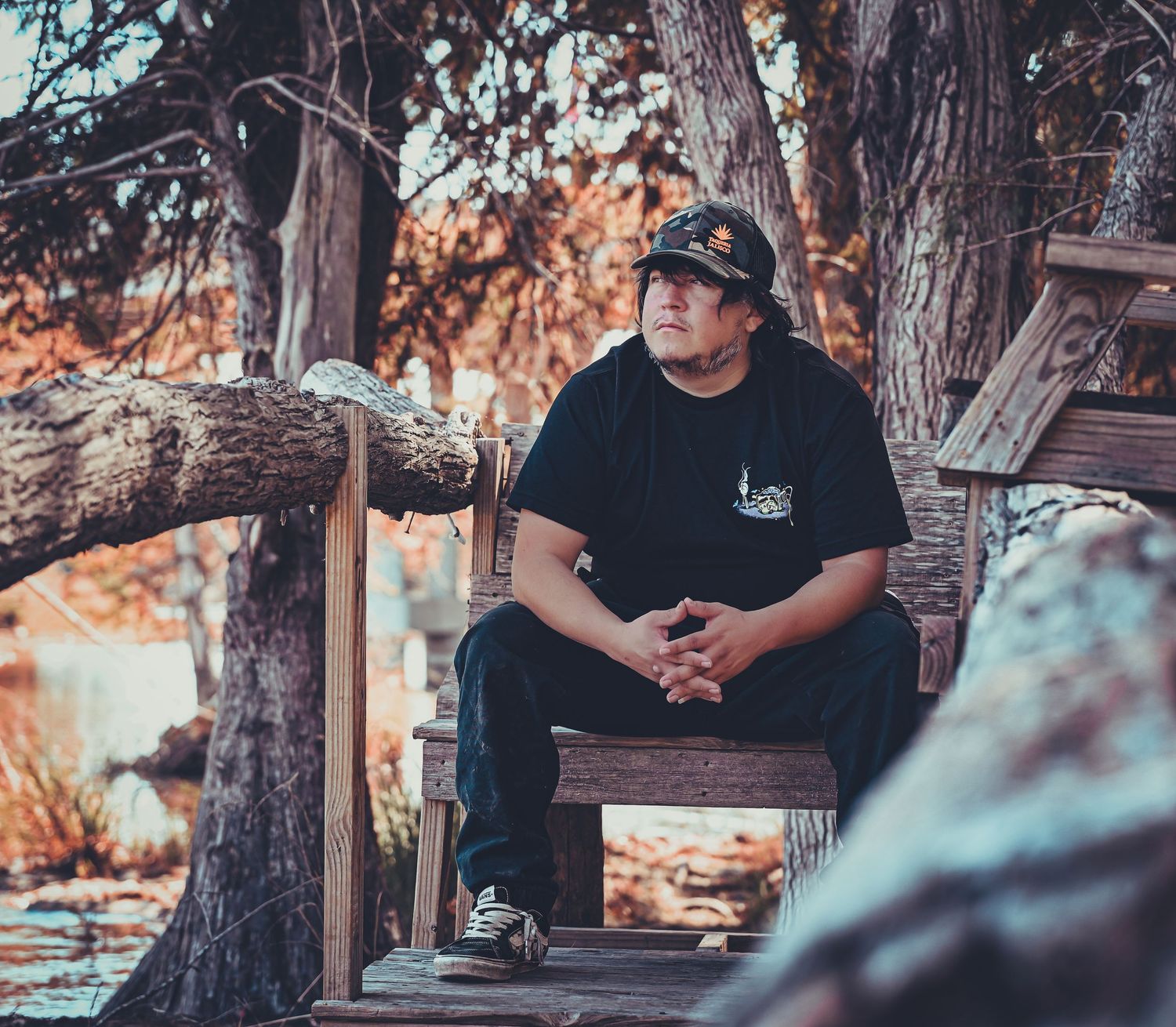 Person in dark clothing seated on rustic wooden furniture in a forest setting.