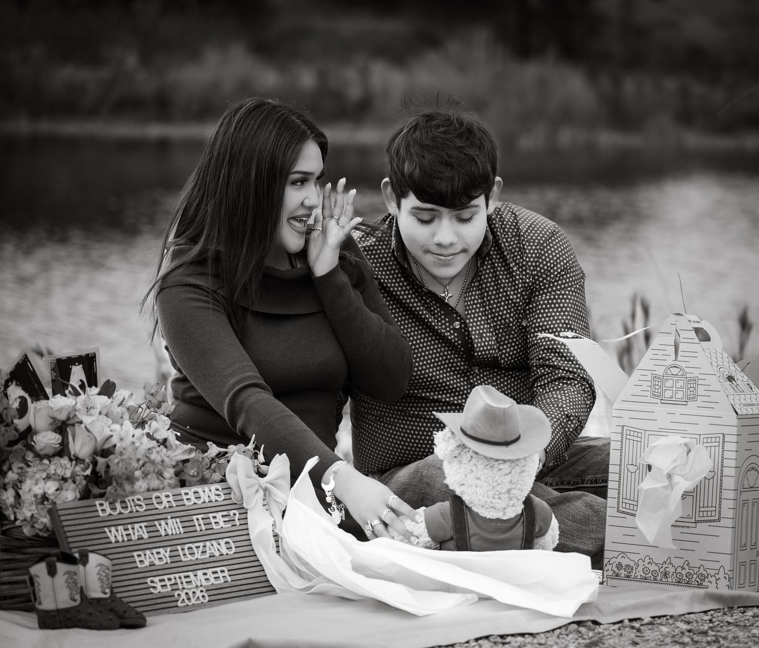Black and white photo of a couple at a gender reveal picnic, showing a sign reading Baby Lozano, September 2021.