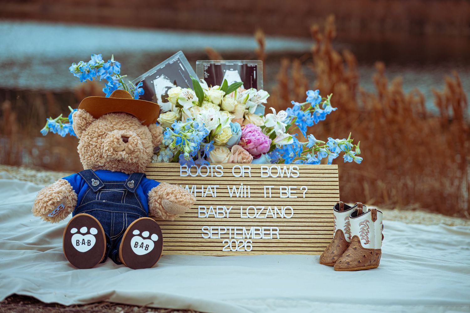 Teddy bear in overalls beside a wooden crate with flowers and a gender reveal sign for Baby Lozano, September 2020.