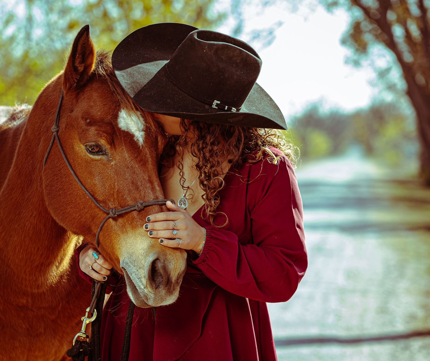 A person in a burgundy jacket shares an affectionate moment with their brown horse in an outdoor setting.