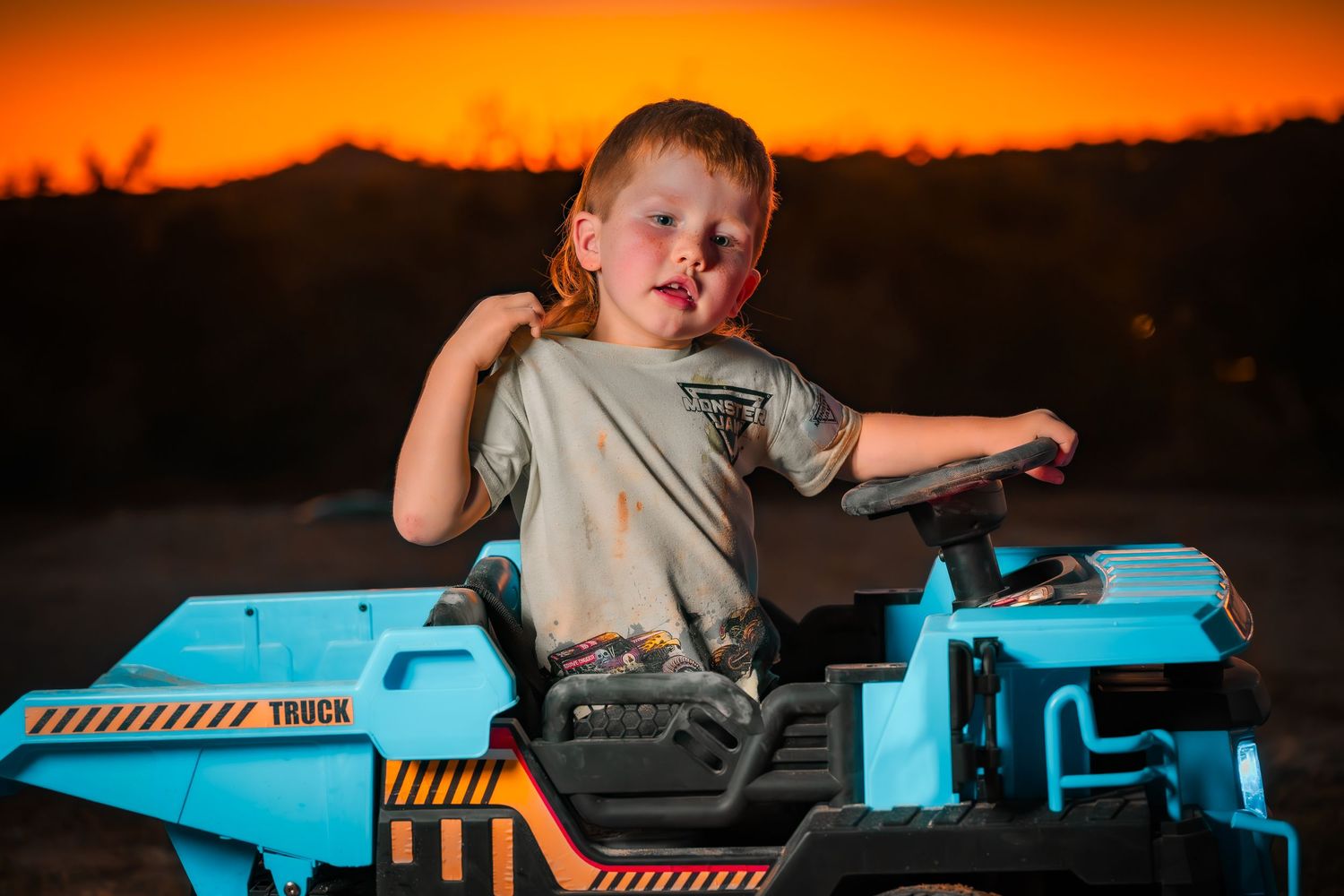 Toy construction truck in bright turquoise blue against dramatic orange sunset sky.