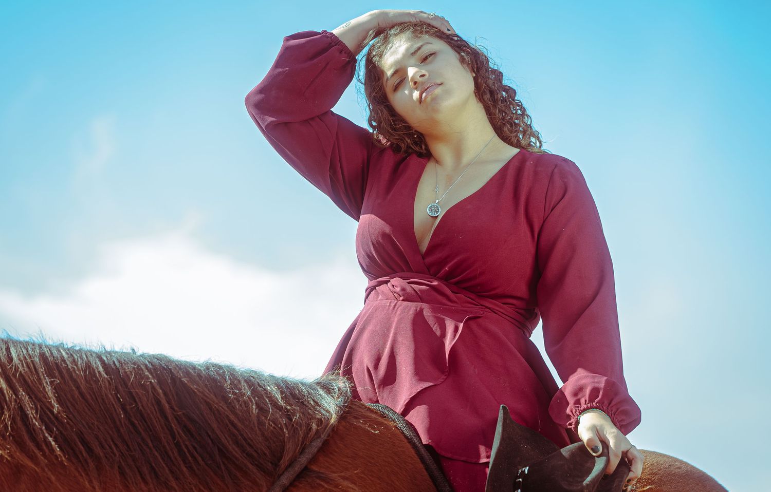 A woman in a burgundy wrap top poses in multiple angles against a bright blue sky background.