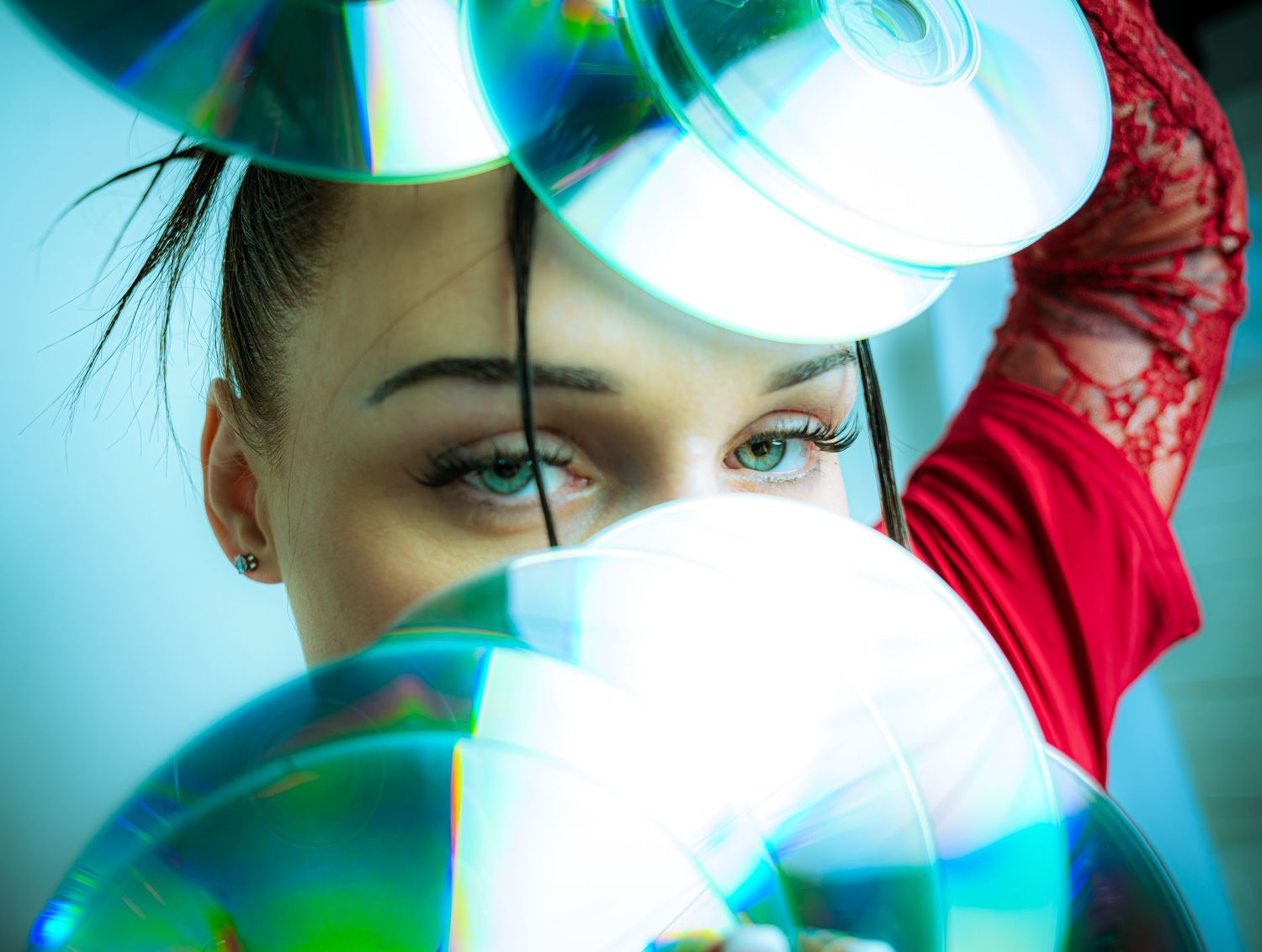 Woman in red lace top peers through colorful iridescent CDs, showcasing vibrant reflections and artistic composition.