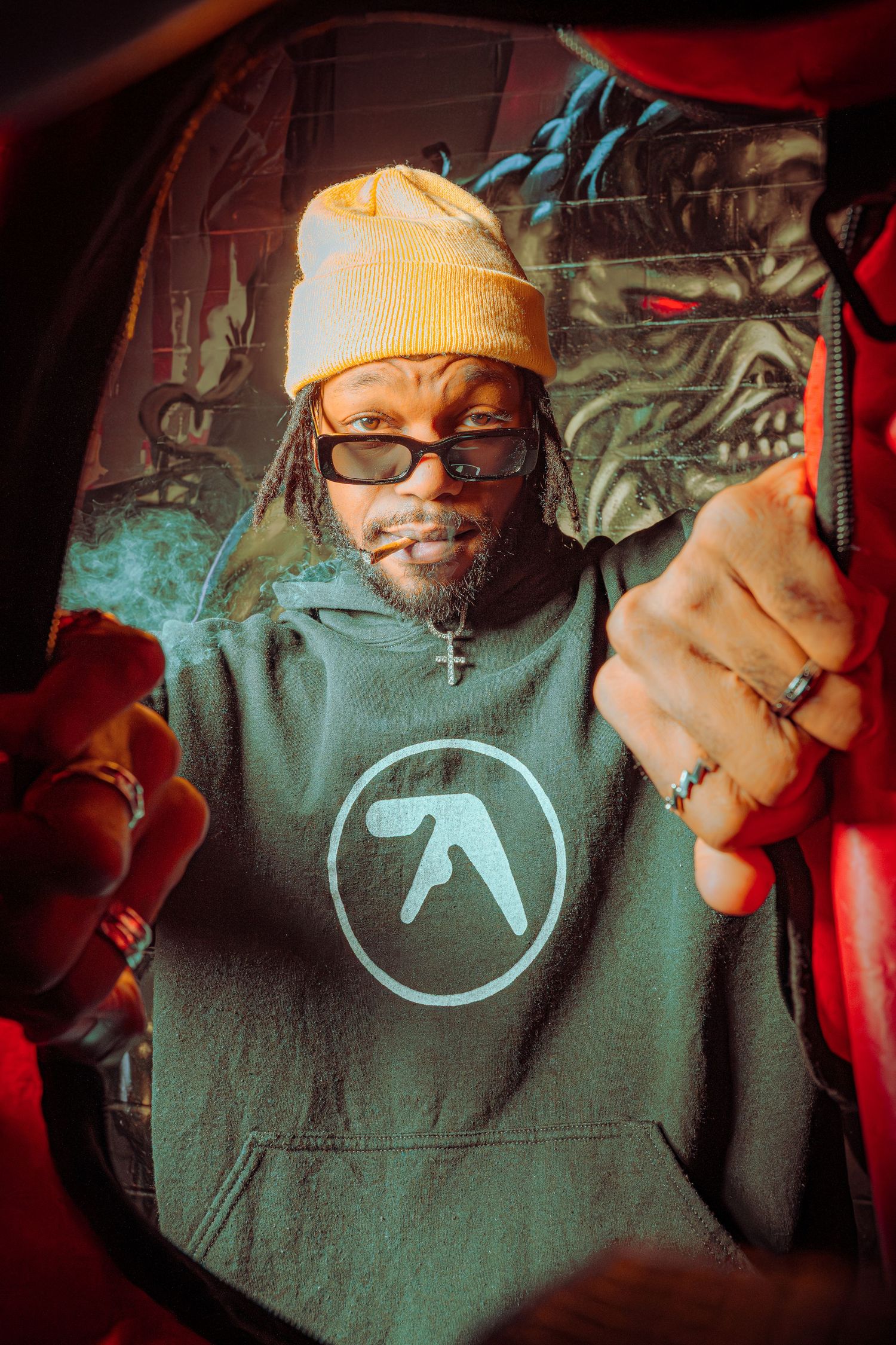 A series of dark moody photos showing someone wearing glasses and a beanie with a black aphex twin logo t-shirt.