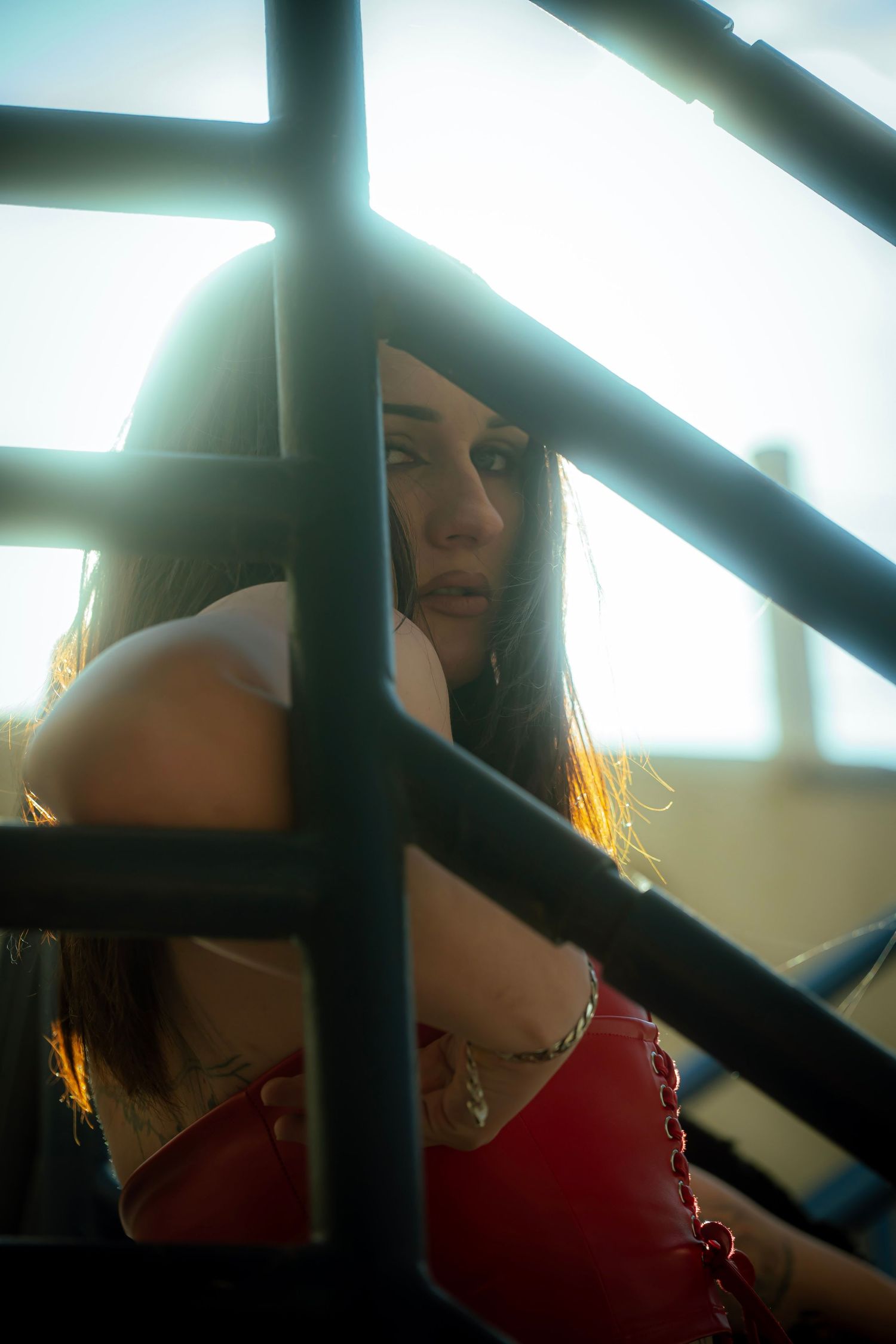 Dramatic portrait through metal bars with person wearing red top in backlit setting.