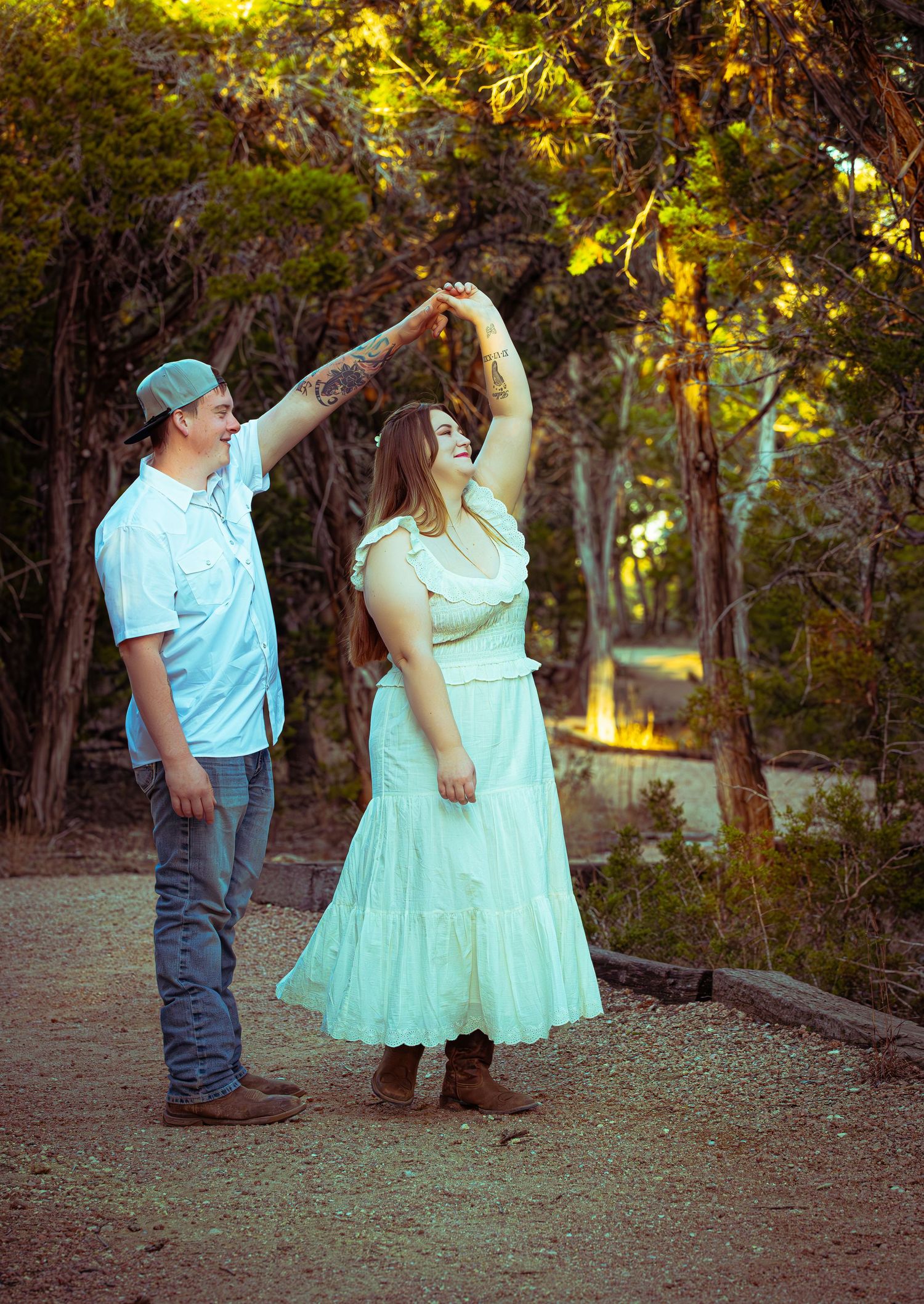 A couple in coordinating mint green and light blue outfits dance together in a sunlit wooded area at sunset.
