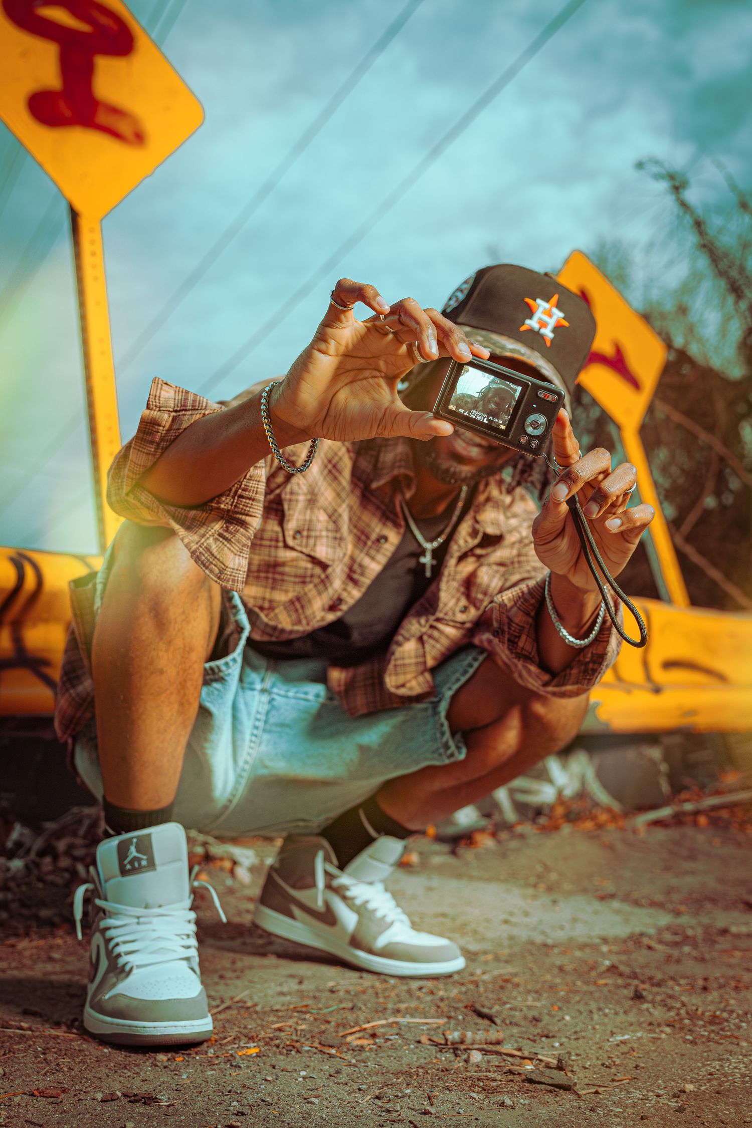 Urban fashion photography with crouched figure in Houston Astros cap, plaid shirt and white sneakers against yellow signs.