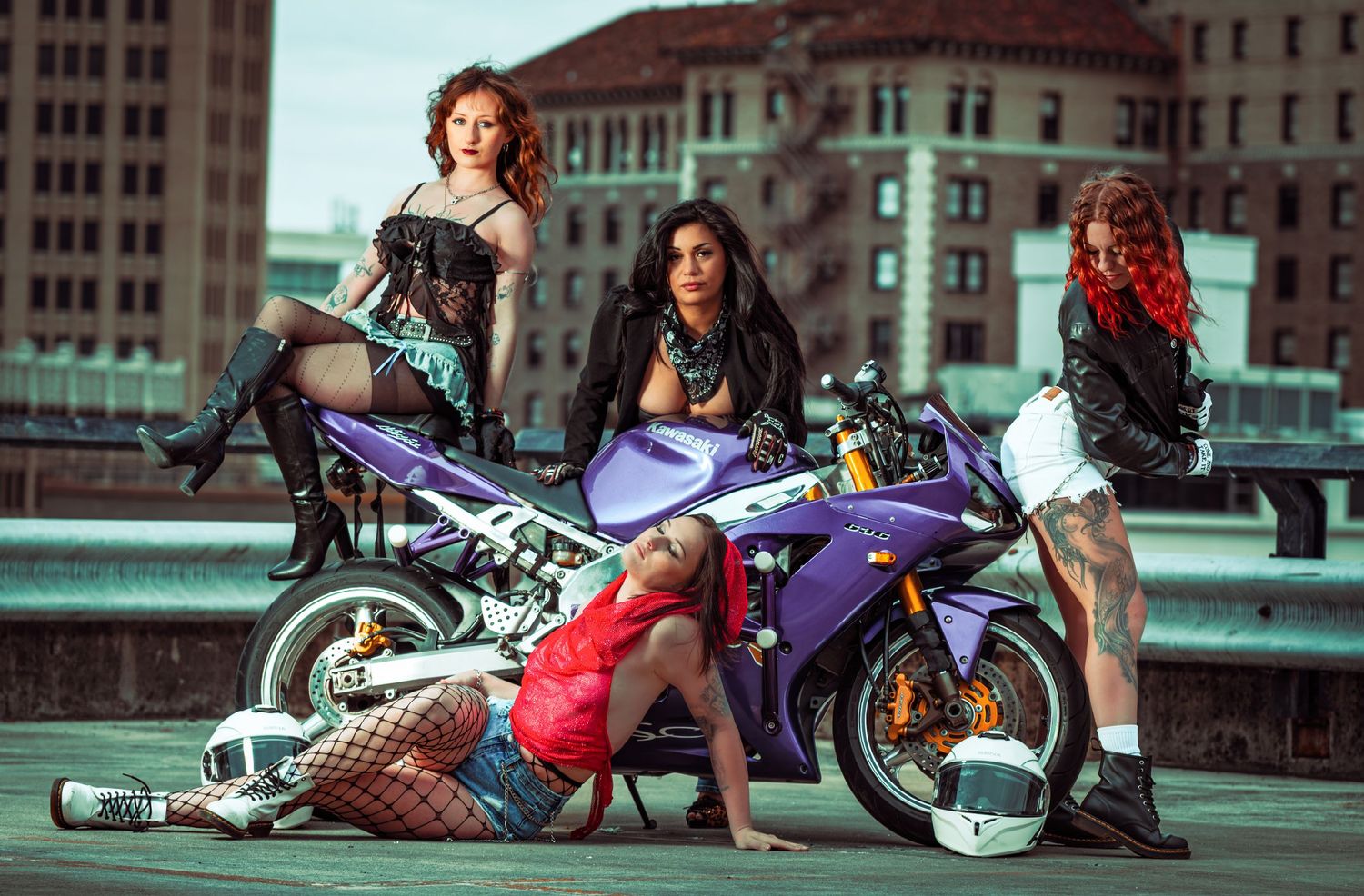 Group of women posing with a purple sports motorcycle on an urban rooftop with city buildings in the background.