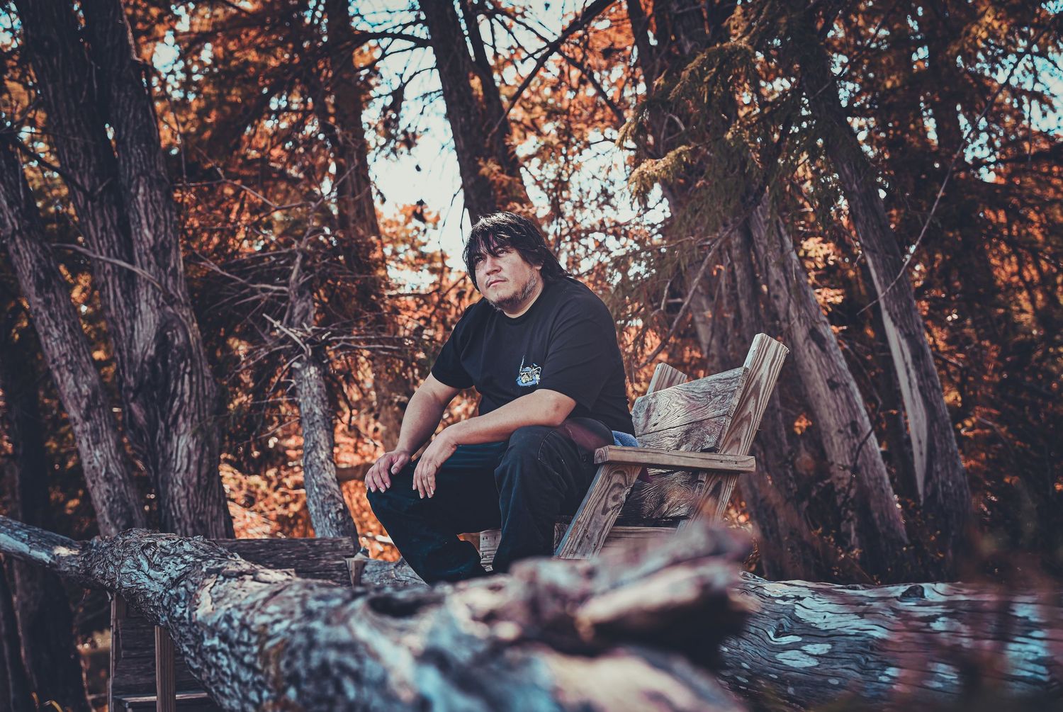 Person sitting on a wooden bench in an autumn forest setting with warm lighting and fallen leaves.
