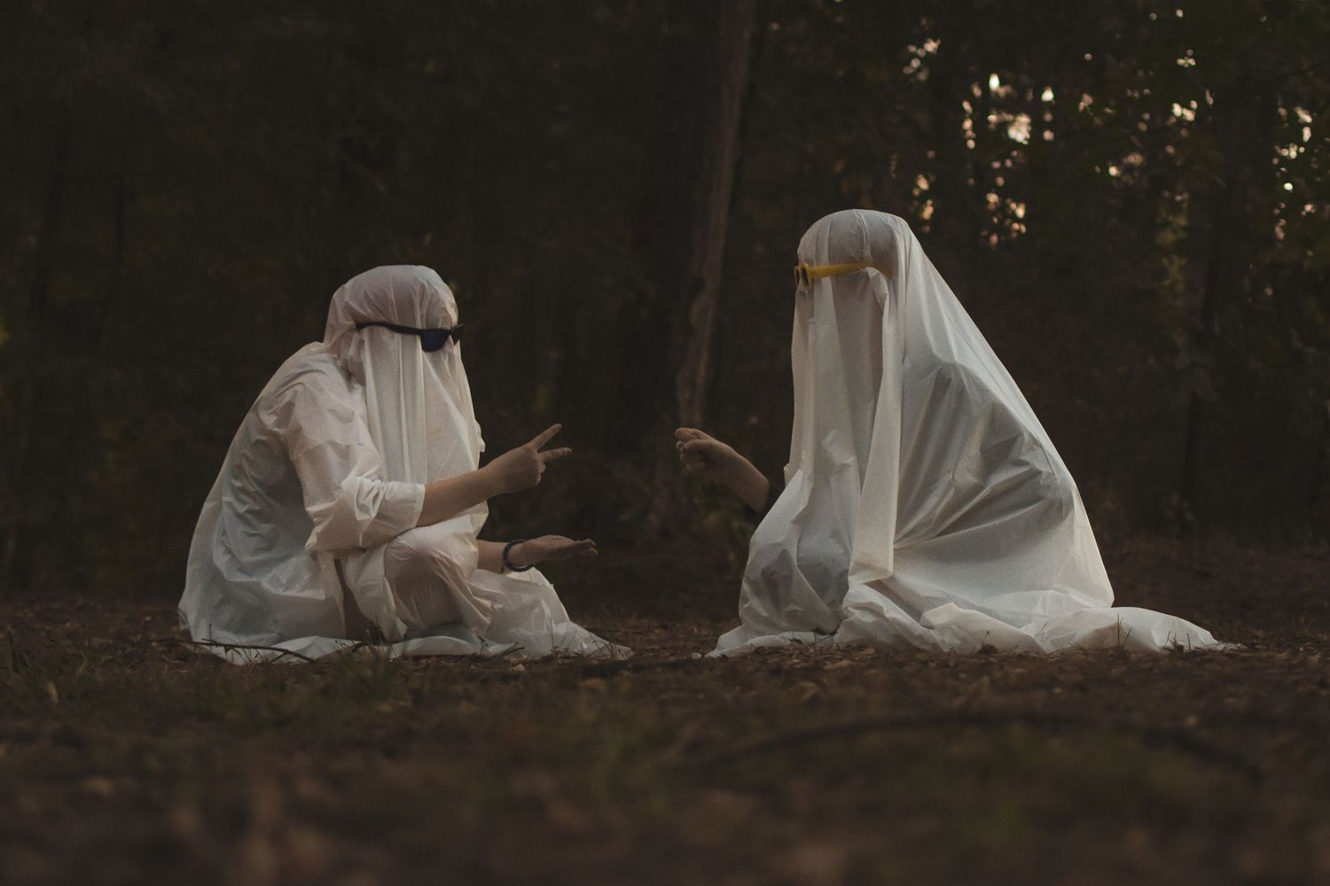 Two people with sheets and sunglasses on pretend to be ghosts playing rock, paper, scissors.