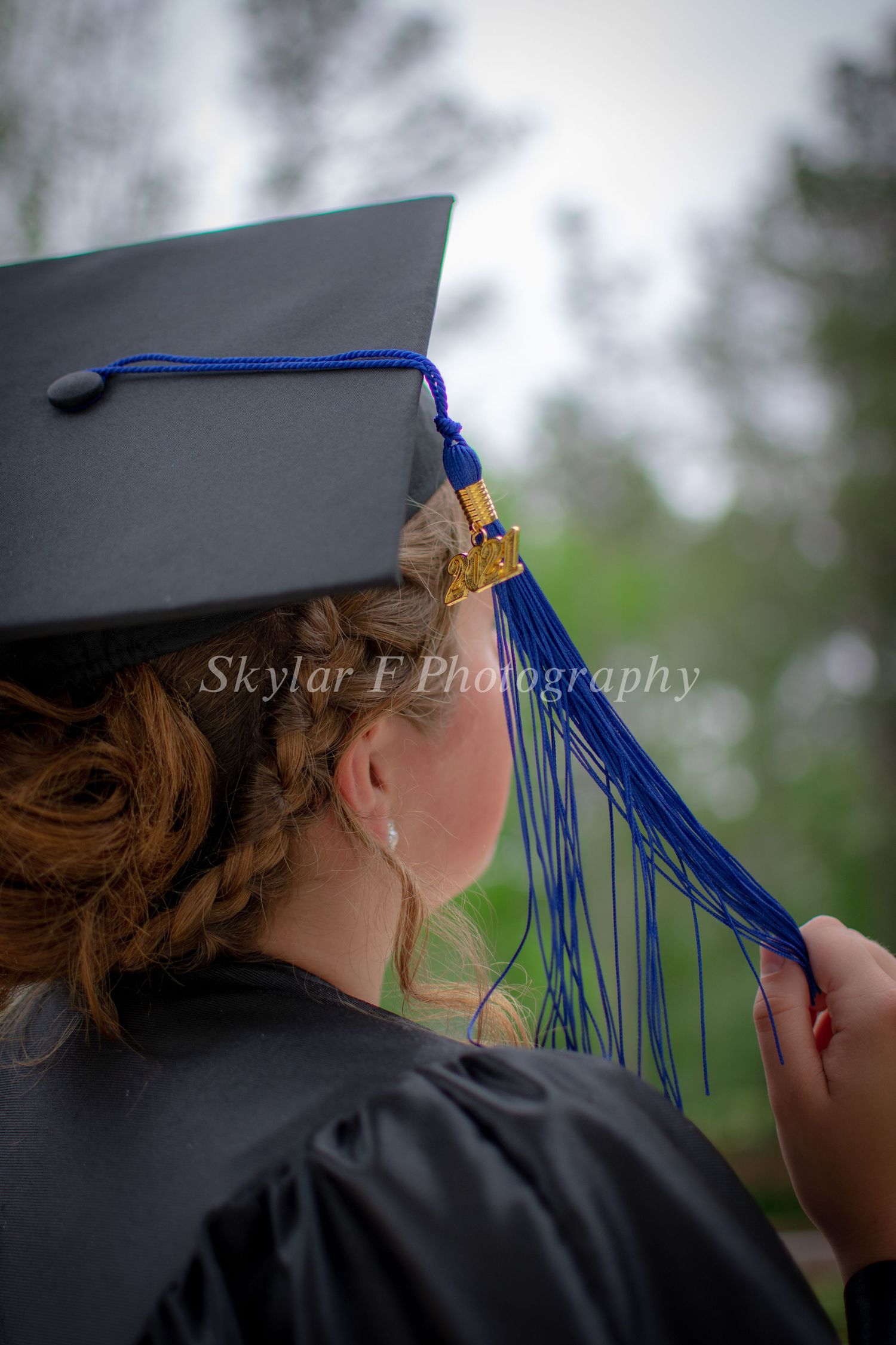 The outline of a girls' head can be seen as she holds the tassel hanging off oh her graduation cap.