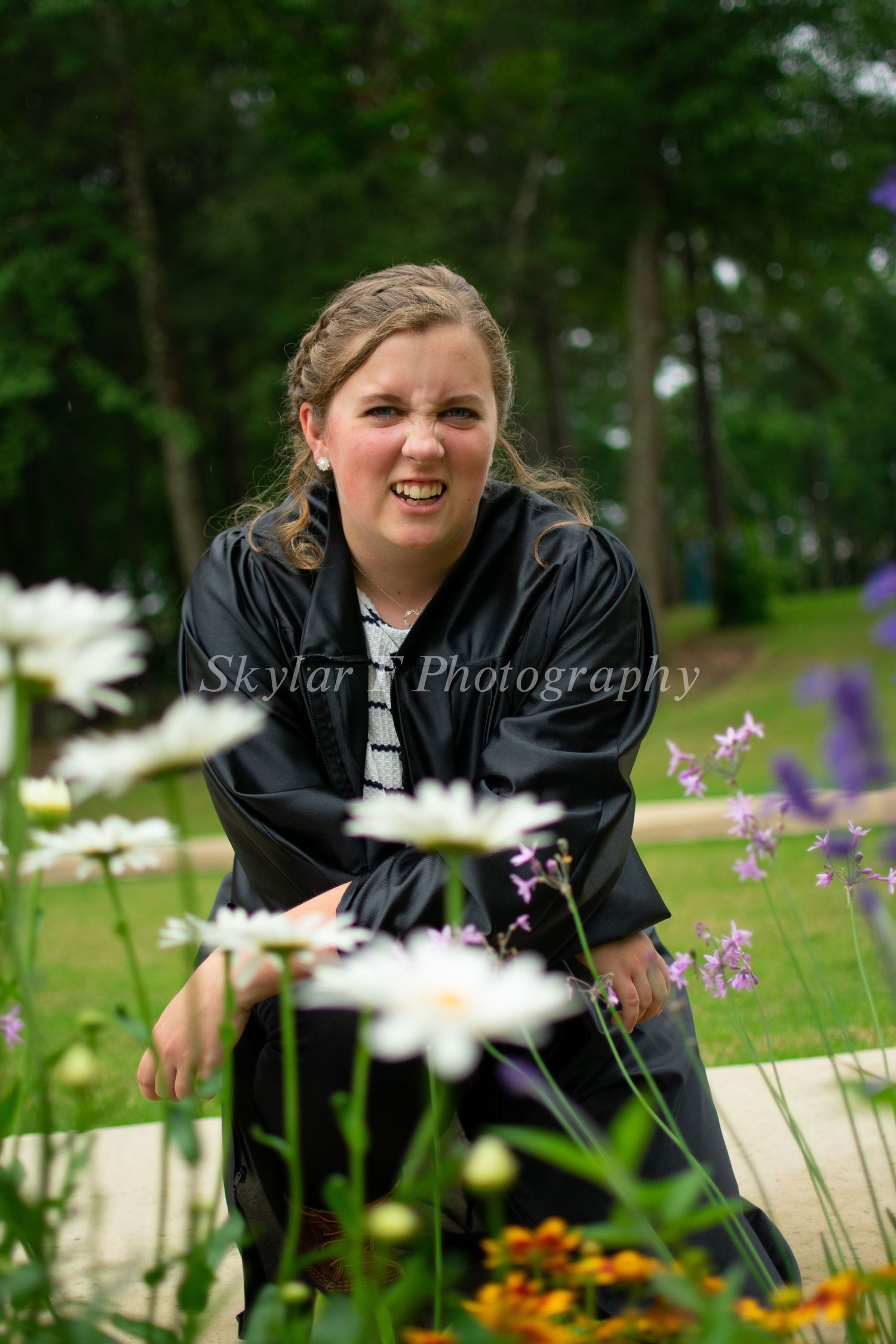 A high school senior poses behind some flowers and makes a silly face at the camera.
