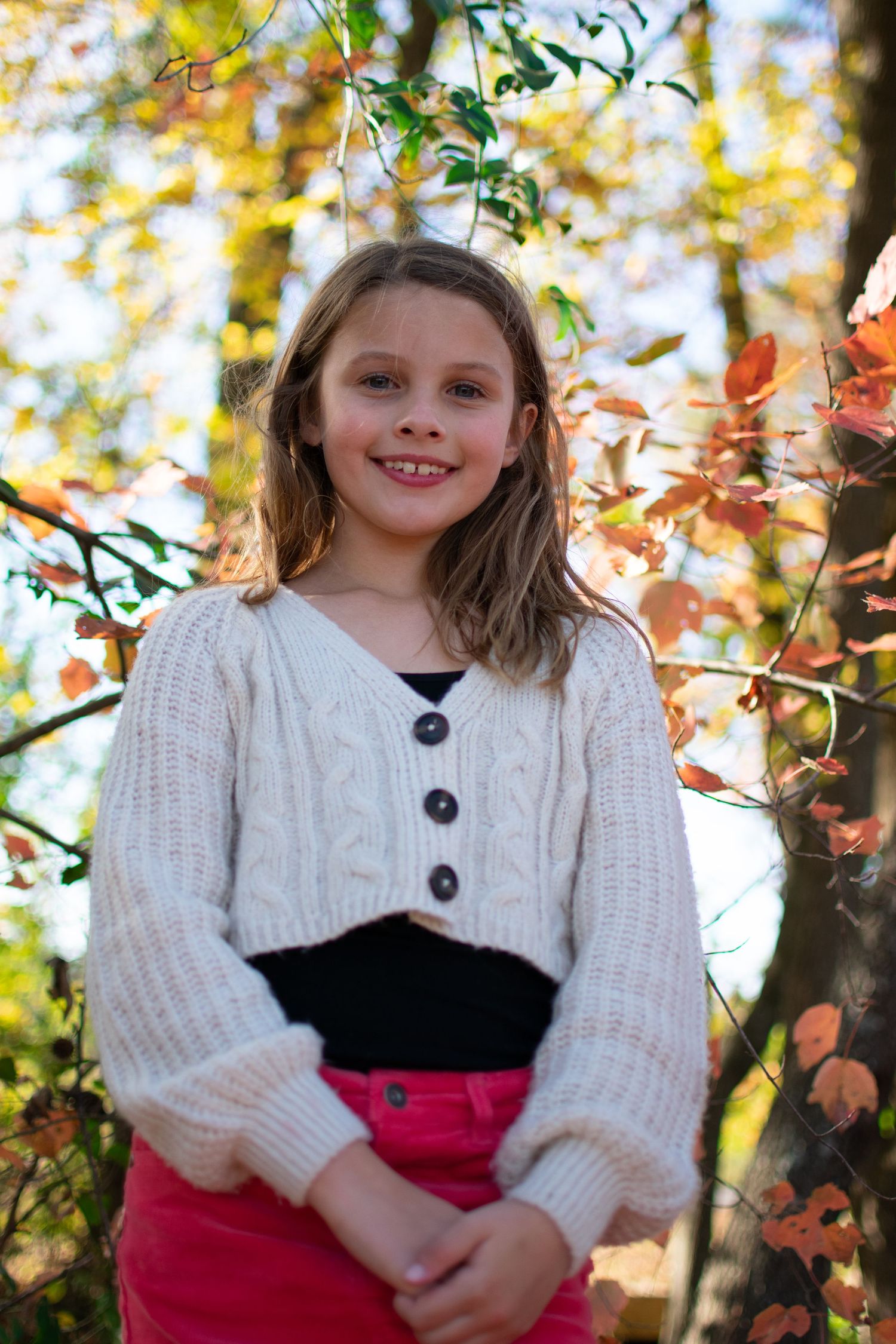 A young girl surrounded by bright fall colors smiles at the camera.
