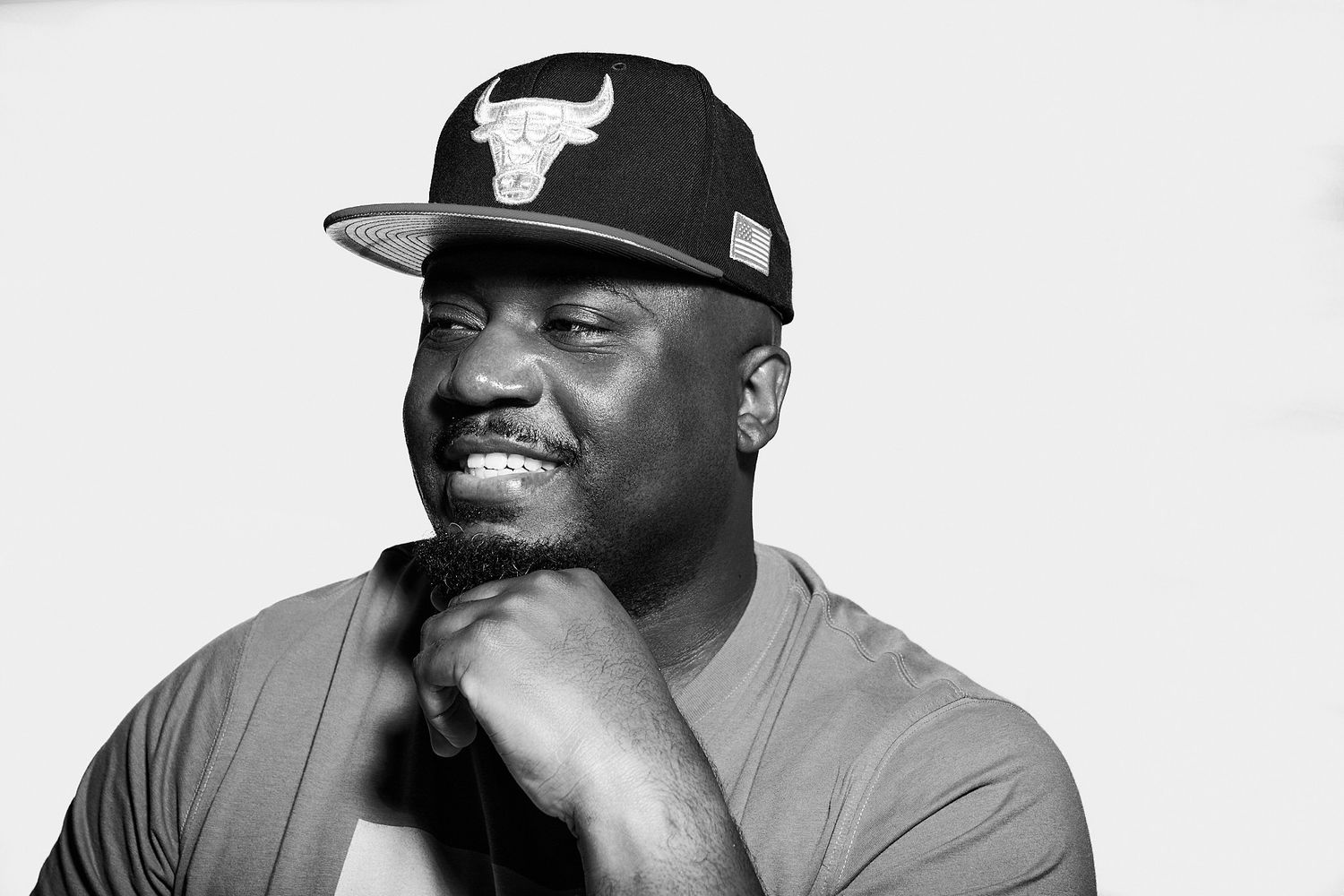 Black and white photo of person in Bulls hat smiling while resting hand on chin.