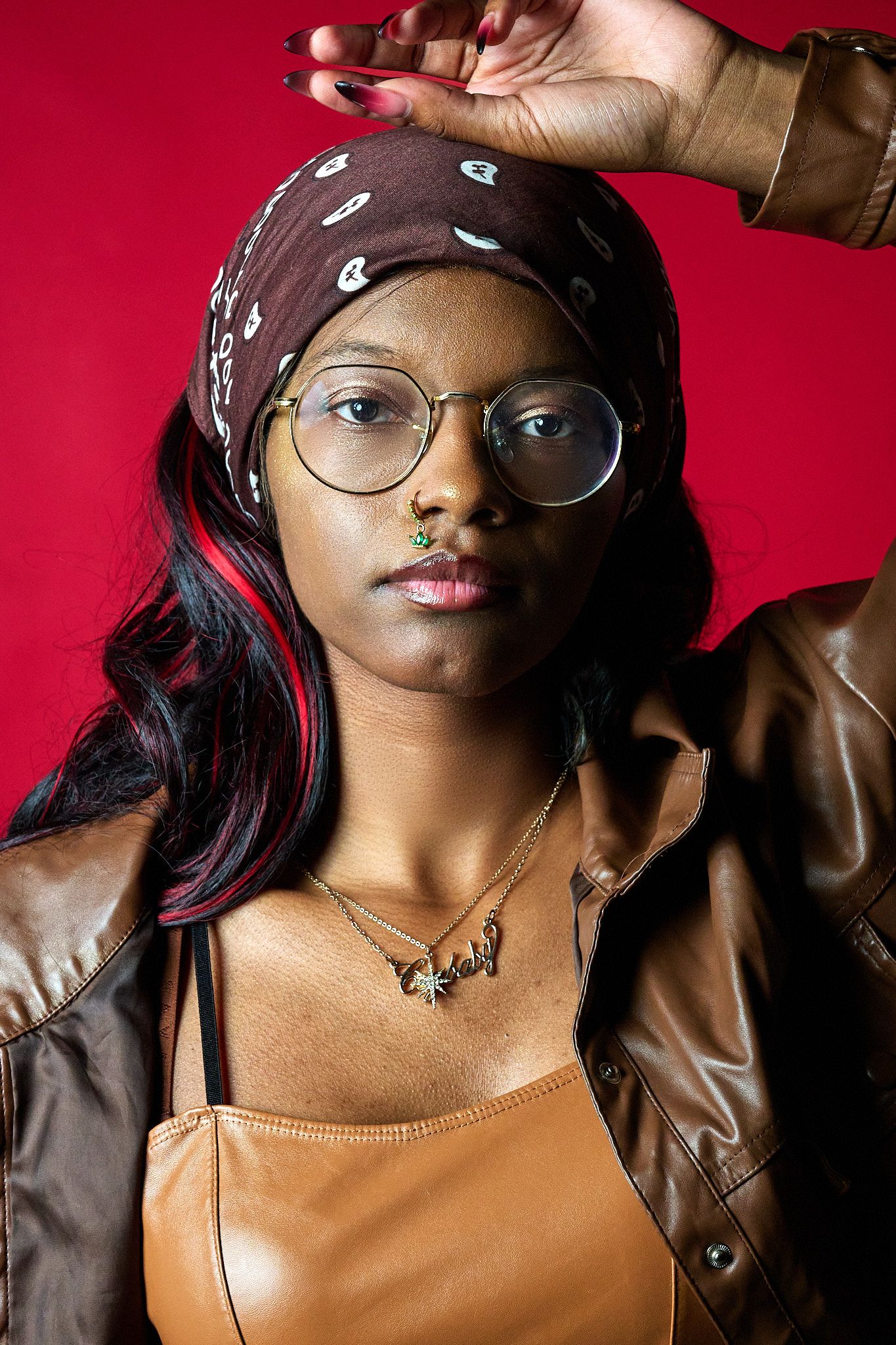 Artistic portrait series against red background showing close-up details of glasses, jewelry and leather jacket styling.