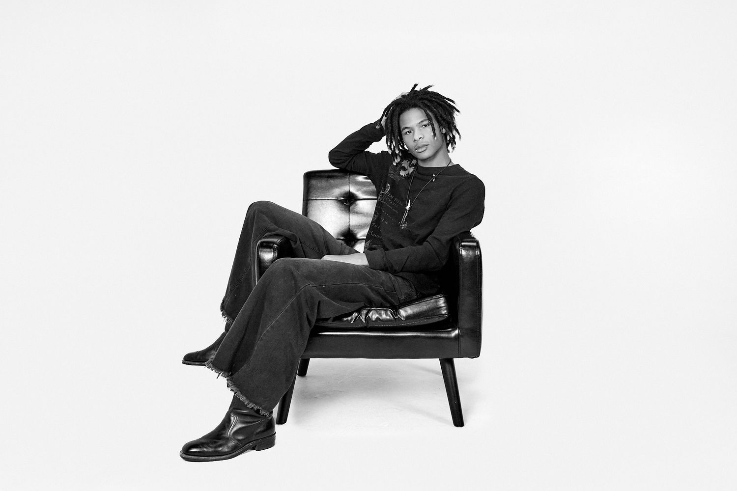A person wearing dark clothing sits on a bench in a minimalist setting with a white background.