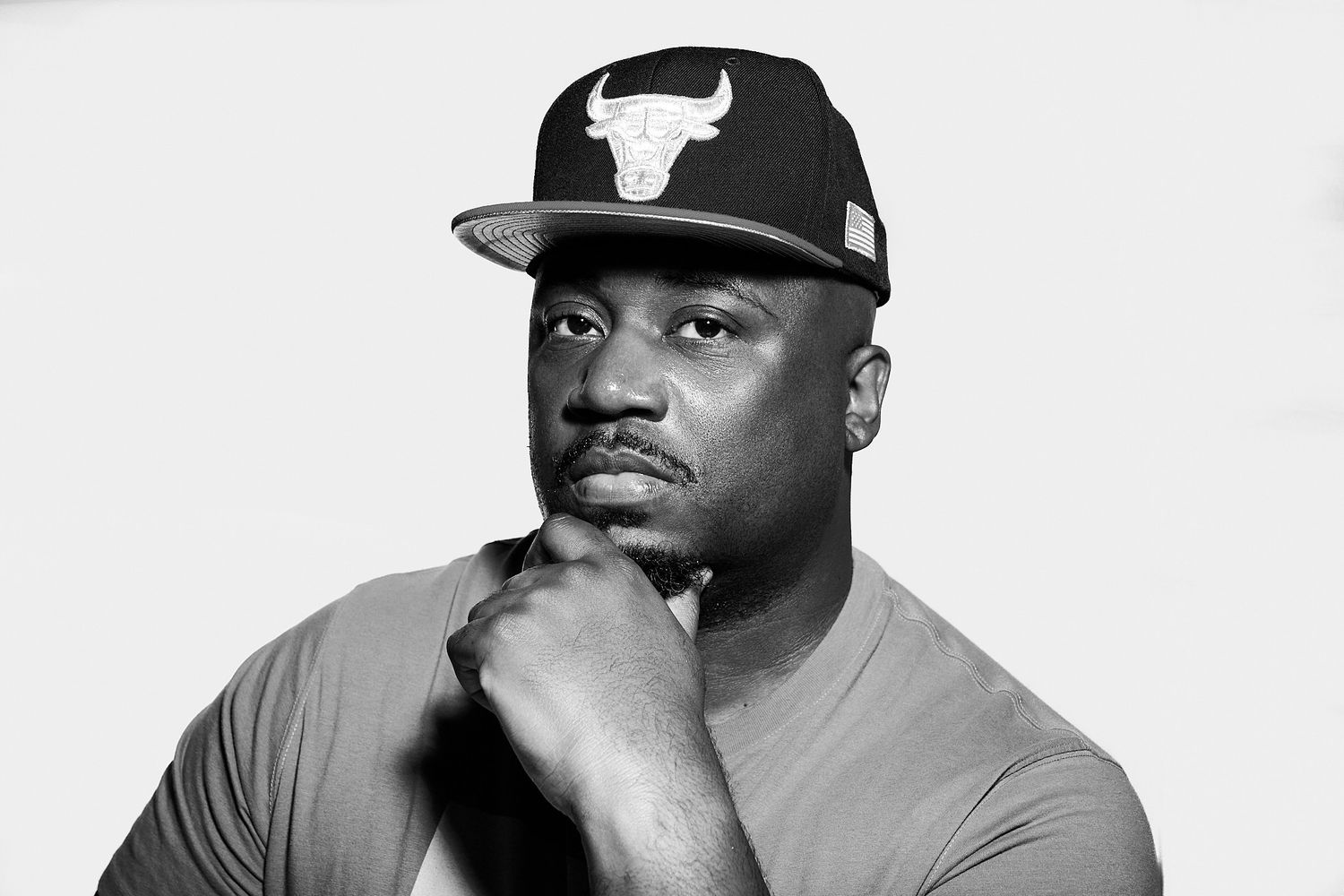 Black and white portrait of person in Chicago Bulls cap with thoughtful expression and hand on chin.