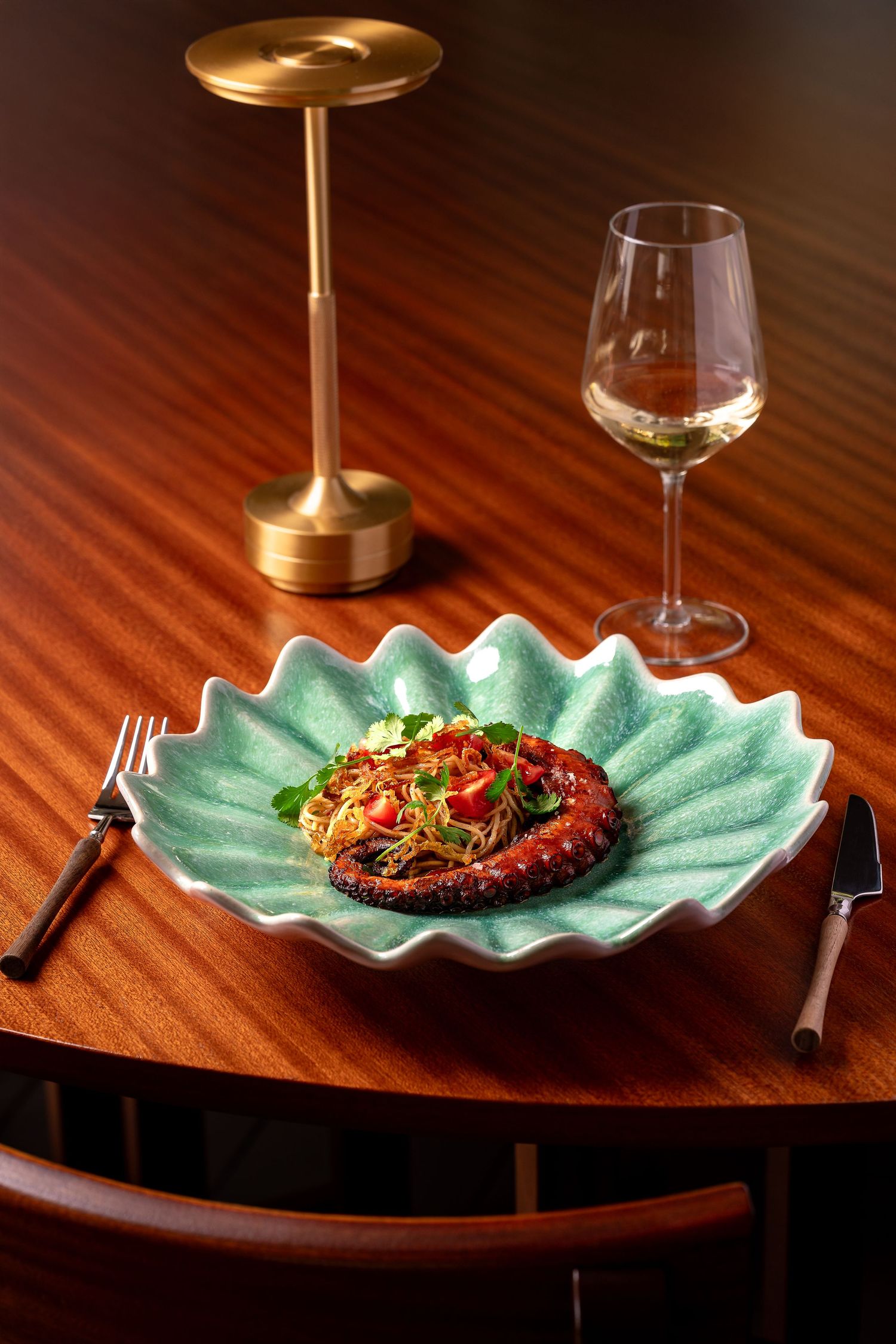 Gourmet dish served on turquoise ceramic plate with gold lamp on wooden table.