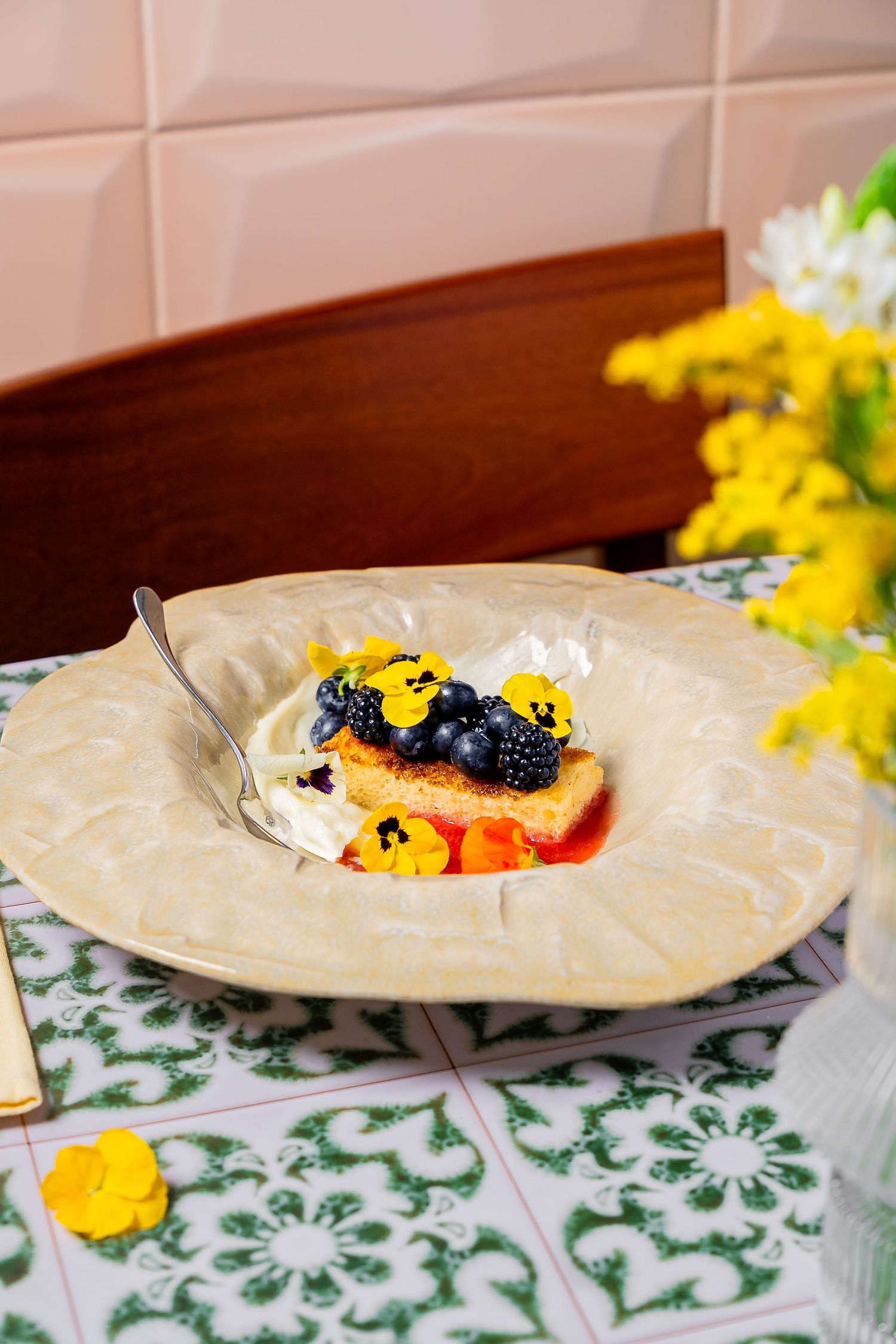 Elegant white plates with colorful food presentation on a green and white floral patterned tablecloth.