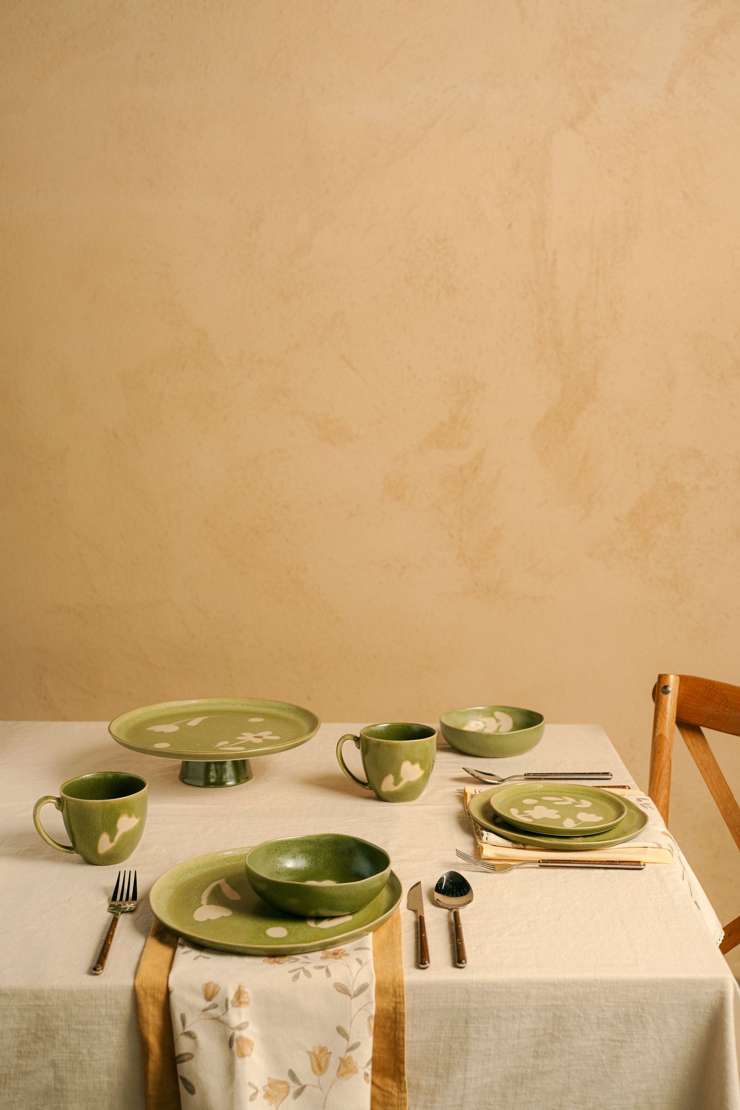 Minimalist table setting with sage green ceramic plates on linen tablecloth.