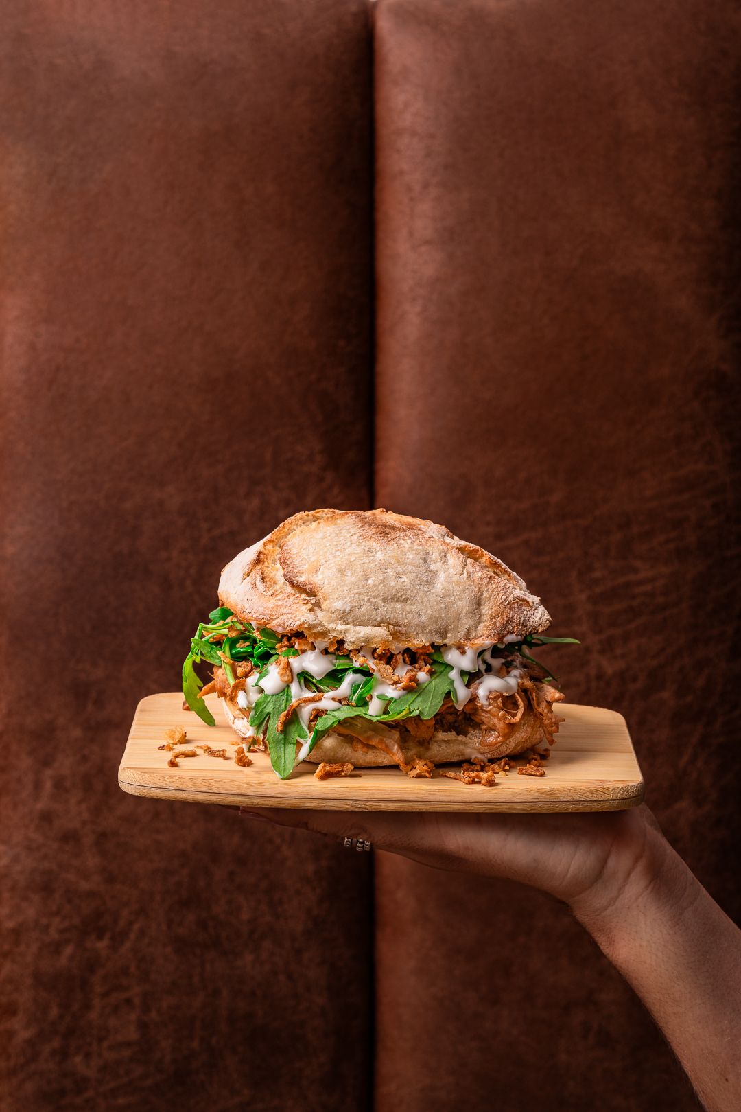 Artisanal sandwich on wooden board photographed in sequence against dark background.