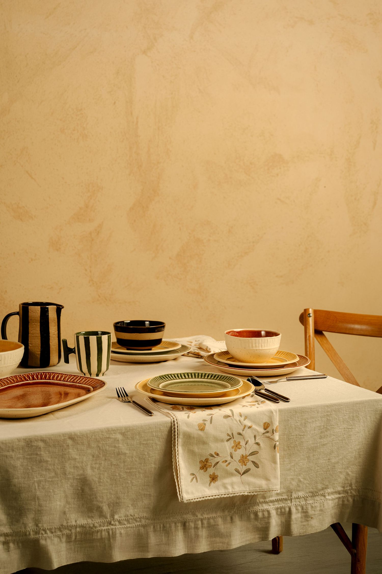 Minimalist table setting with white tablecloth, plates and pitcher in warm tones.
