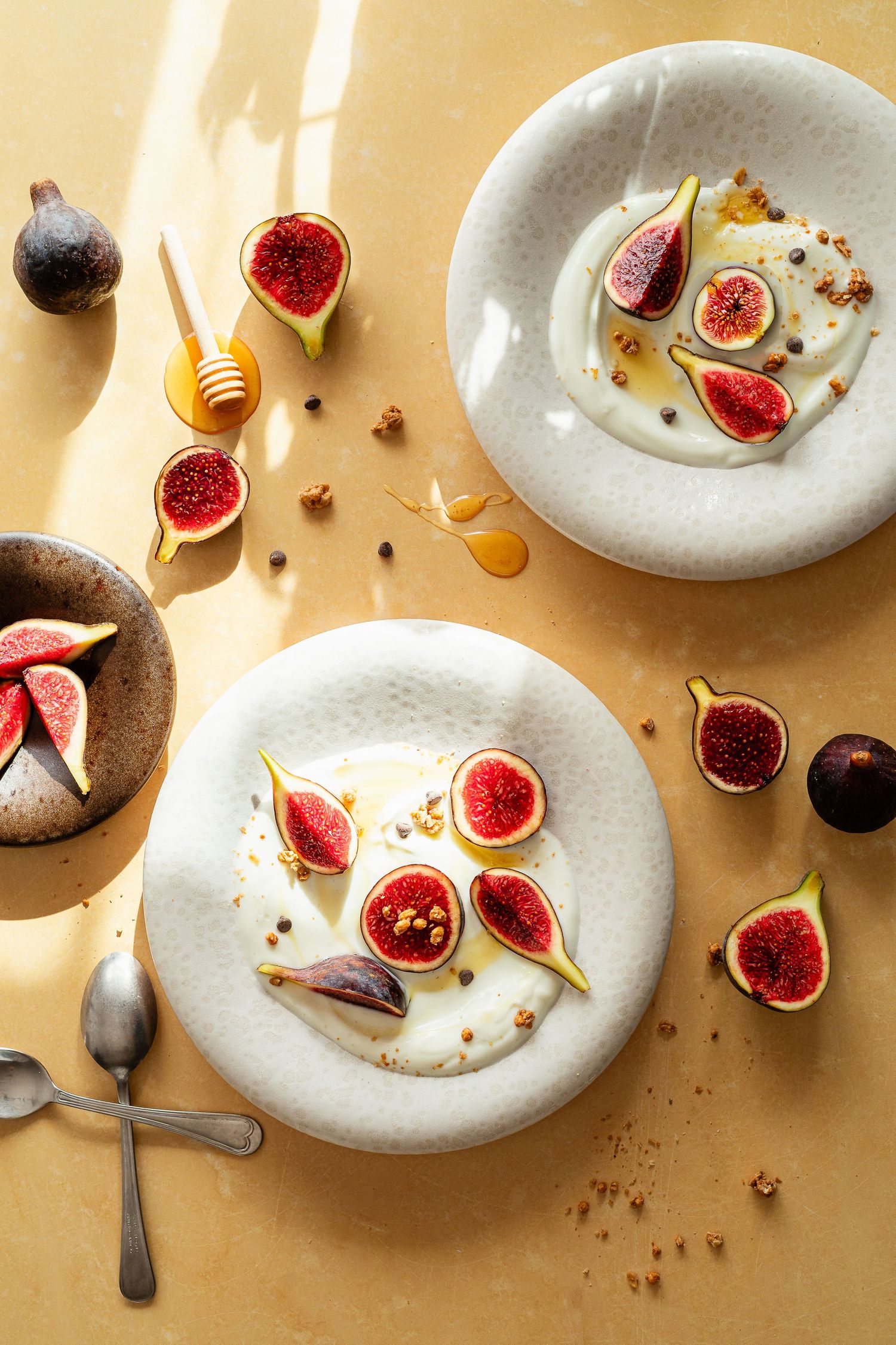 Fresh figs and honey artistically arranged on white ceramic plates in natural sunlight.