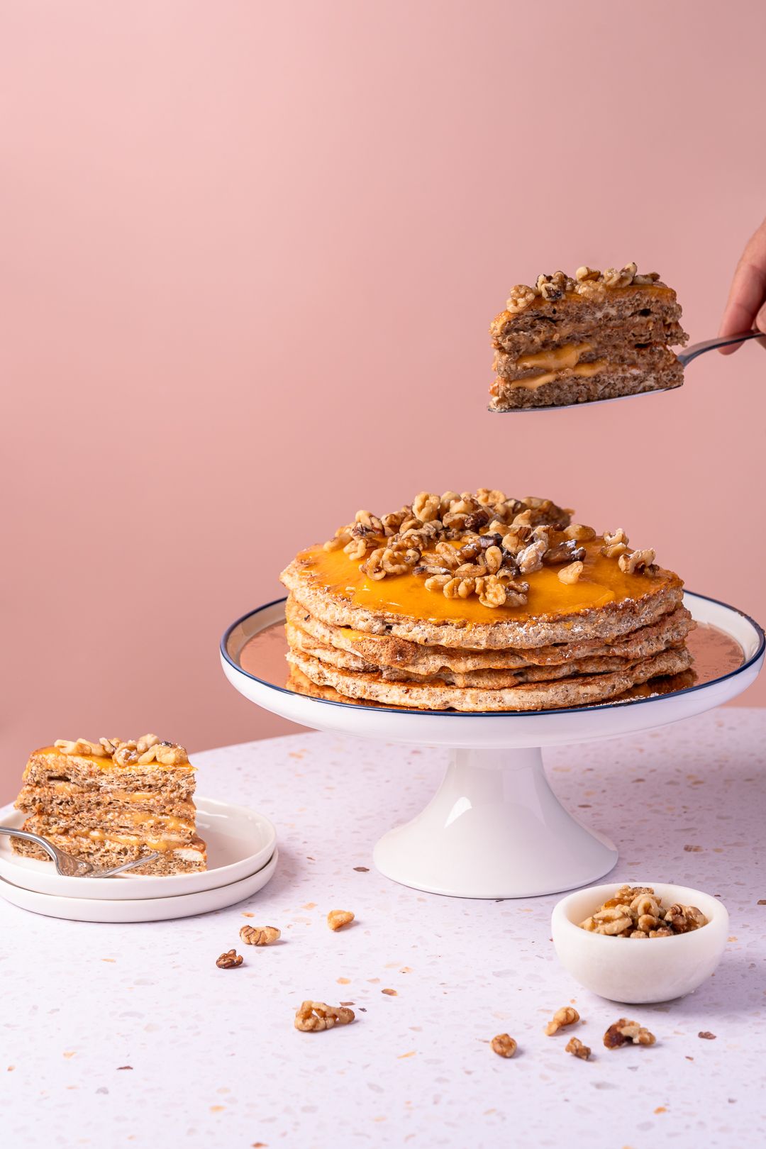 Caramel pecan layered cake being served on white plate against pink background.