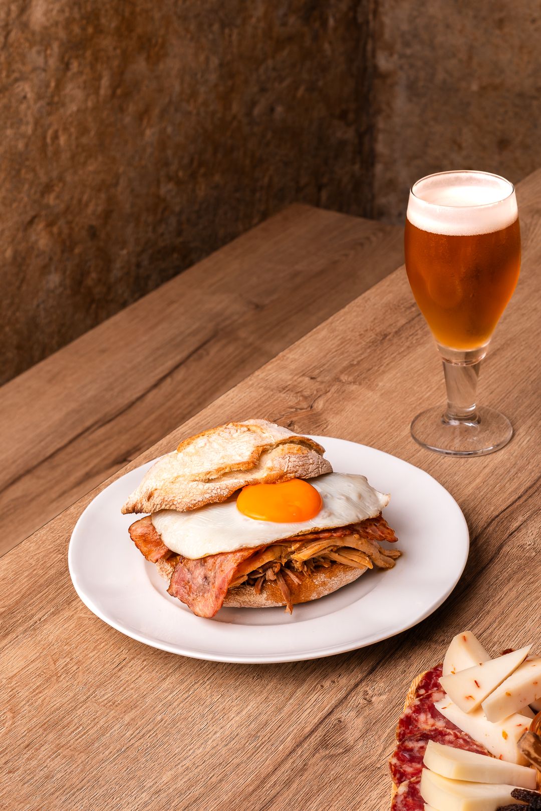 Sandwich with beer pairing on wooden table in rustic setting.